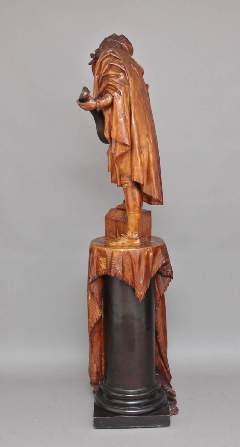 An outstanding 19th century Italian carved wood sculpture of a bearded troubadour playing a mandolin standing on a draped pedestal with one foot on the pedestal and the other on a casket, carved in limewood by the famous Italian wood carver