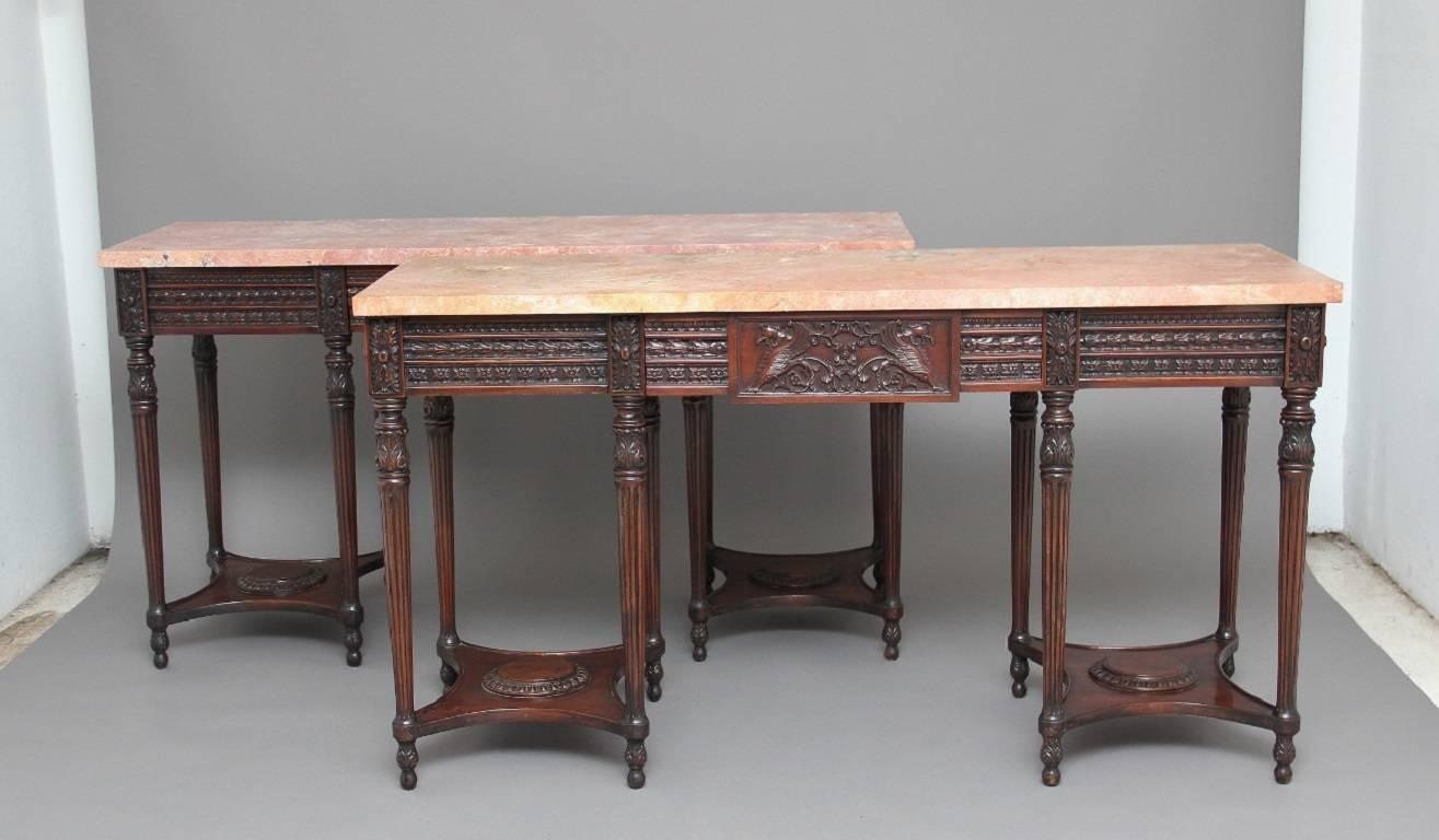 A pair of early 20th century mahogany and marble top console tables in the Adams style, the console’s having pink flecked marble tops, with a profusely carved frieze below with carved patraes and a single drawer at the centre, the frieze also having