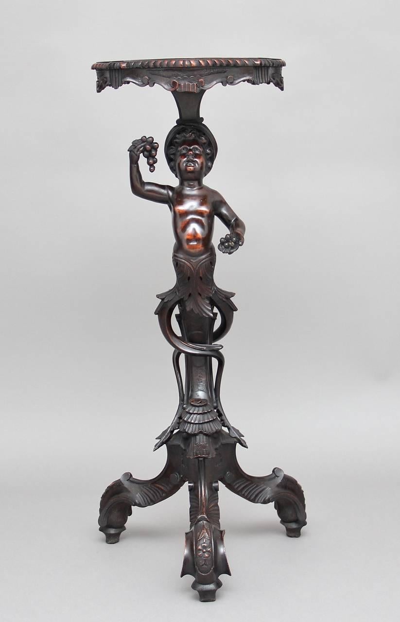 19th century Italian wonderfully carved walnut torcher / stand depicting a boy holding a bunch of grapes whilst holding a tray on his head, supported on a highly carved decorative tri form base, circa 1870.