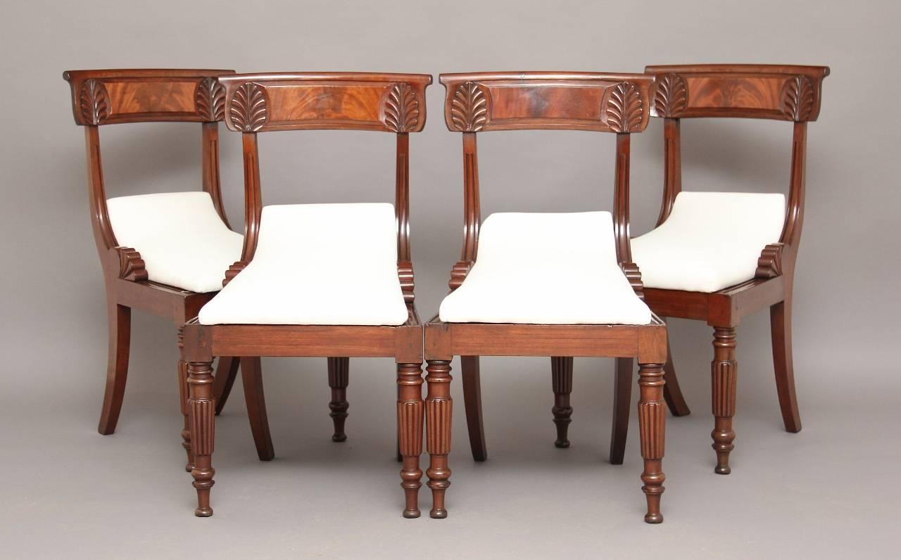 A set of four mahogany dining chairs with carved back rail upholstered in a calico seat with turned front legs and swept back rear legs.