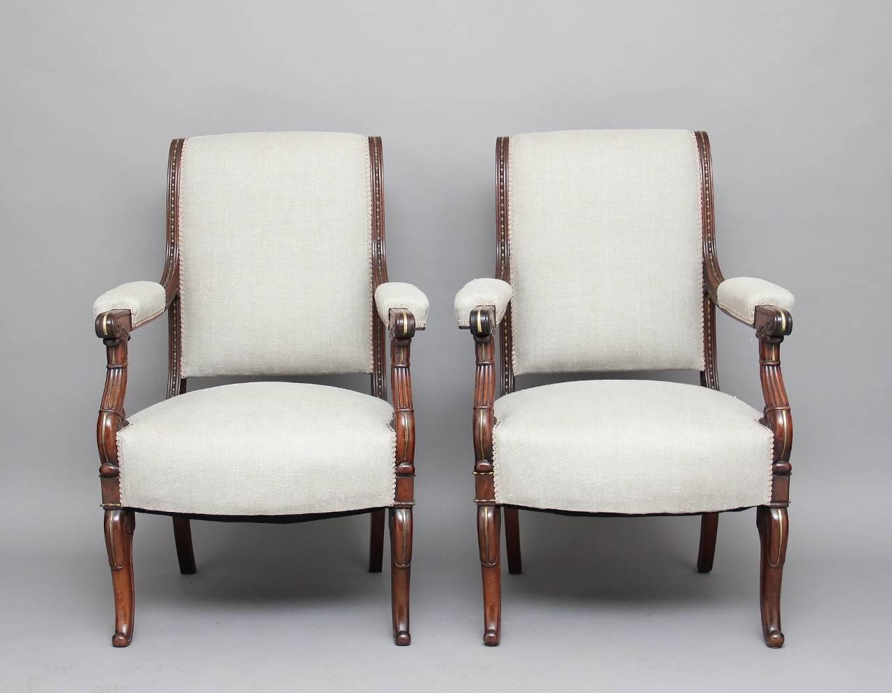 A remarkable and unusual pair of early 19th century French rosewood and brass inlaid armchairs, upholstered in a grey linen fabric, with a shaped and scrolled back, the padded arms with carved and readed supports with nice scroll decoration,