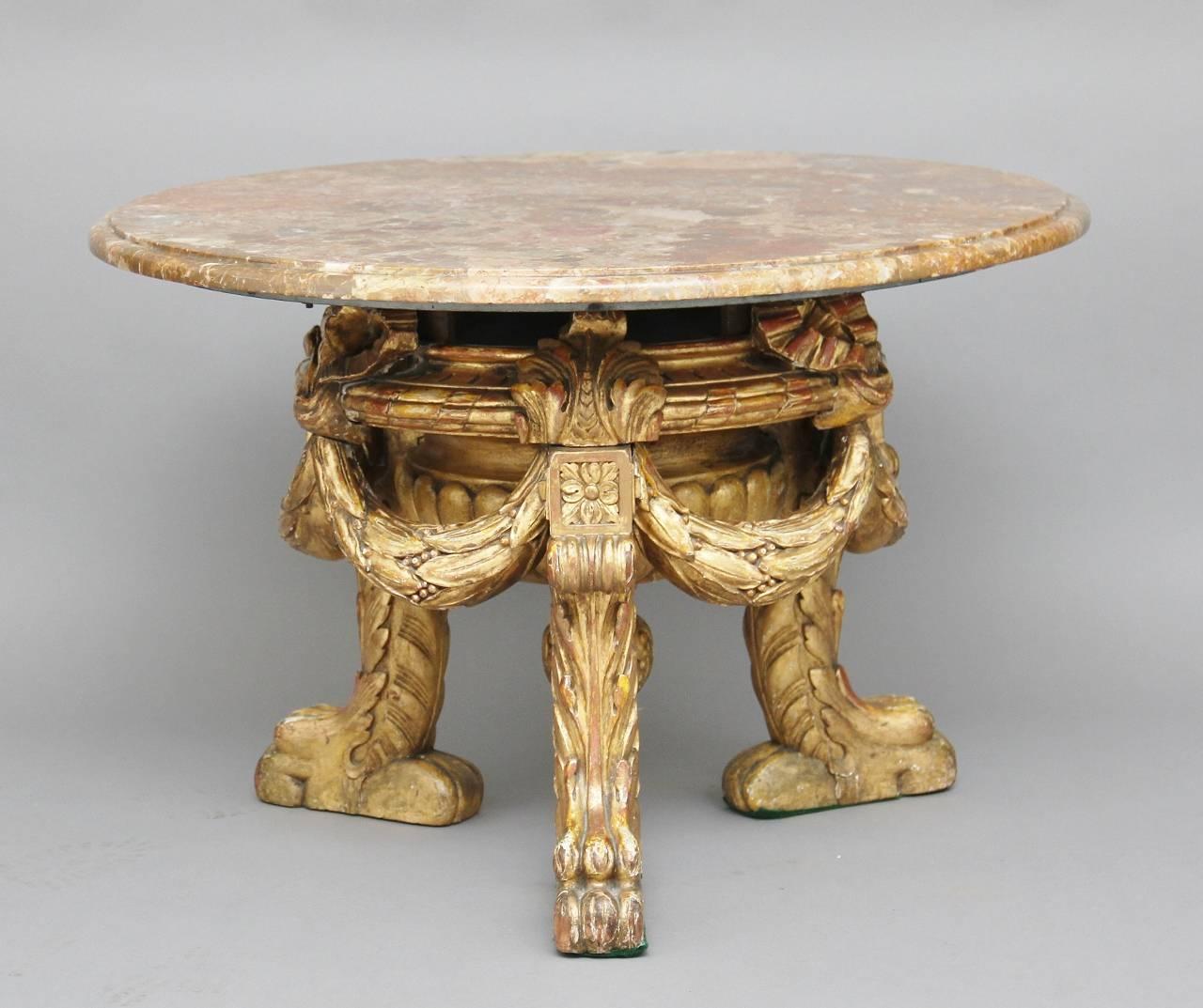 Mid-20th century Italian occasional / coffee table with a veined marble top with a moulded edge, the base made from giltwood which is heavily carved, decorated with swags which are united with the legs, standing on lion feet, circa 1960.