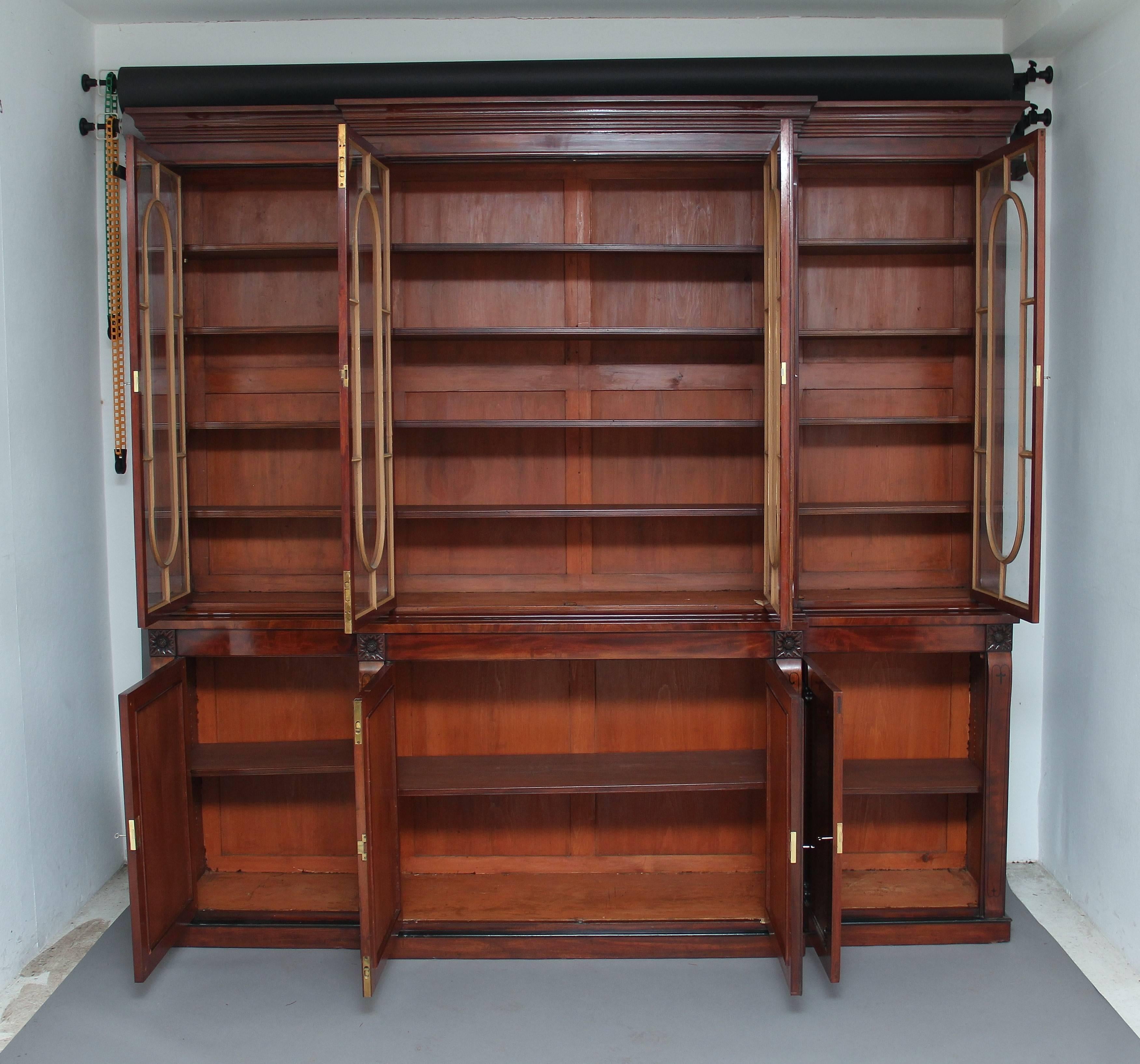 Early 19th century mahogany breakfront bookcase, the top having a stepped moulded cornice with four glazed doors below with nicely shaped astral bars, each door decorated with carved patraes in each corner, the doors opening to reveal four