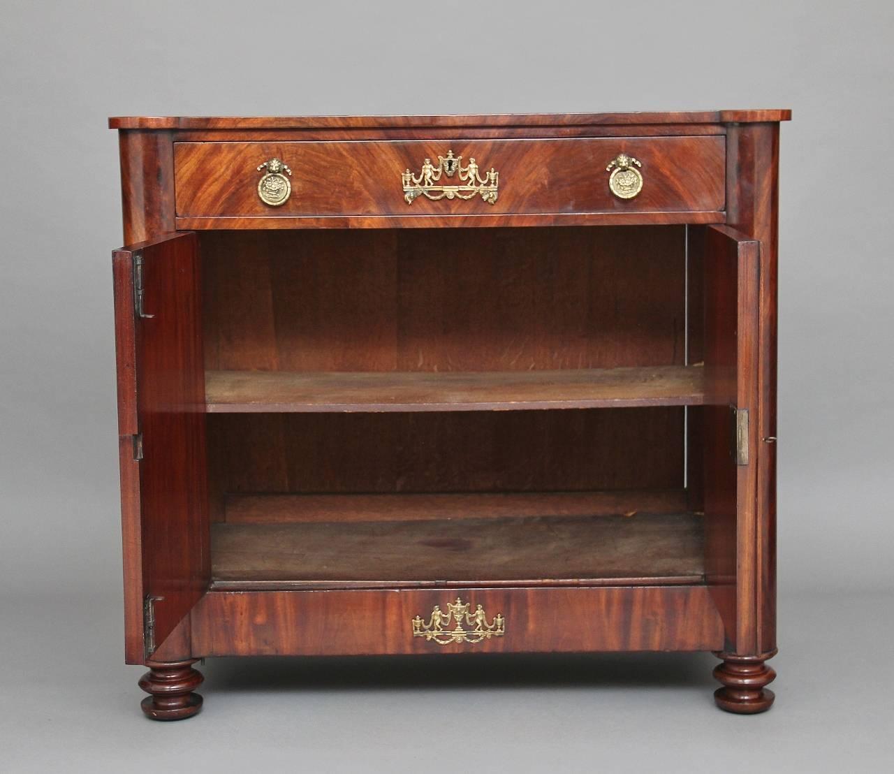 19th century French mahogany cabinet, having a single drawer above a two-door cupboard with a single shelf inside, the drawer and doors having brass mask handles, oval escutcheons and applied decoration, flanked either side by half columns,