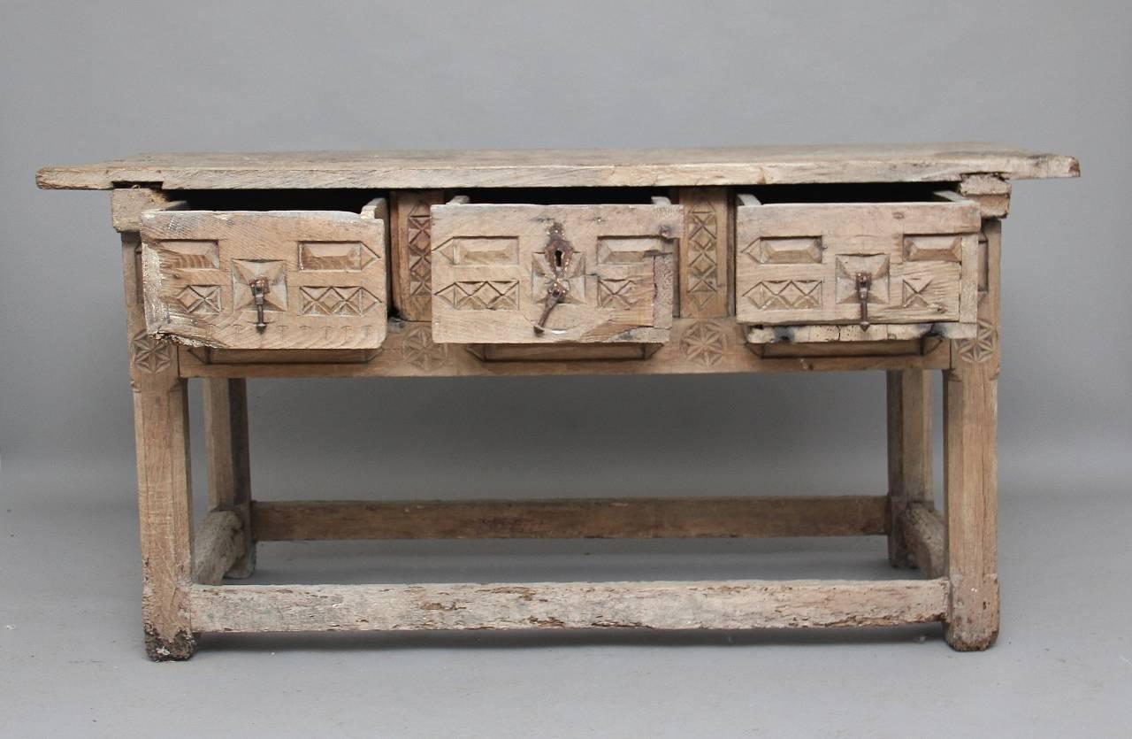 Mid-17th century Spanish chestnut side or serving table with three chip carved drawers, standing on chamfered legs united by stretchers, the drawers looking to have the original iron drop handles, with the middle drawer having a lovely iron lock and