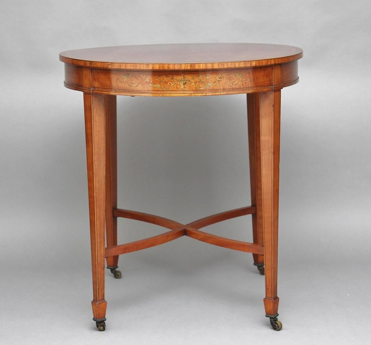 table d'appoint en bois de satin marqueté du XIXe siècle, avec un plateau de forme ovale, le tablier en dessous abondamment marqueté sur toute sa surface, reposant sur des pieds fuselés avec des pieds en forme de bêche et des roulettes en laiton,