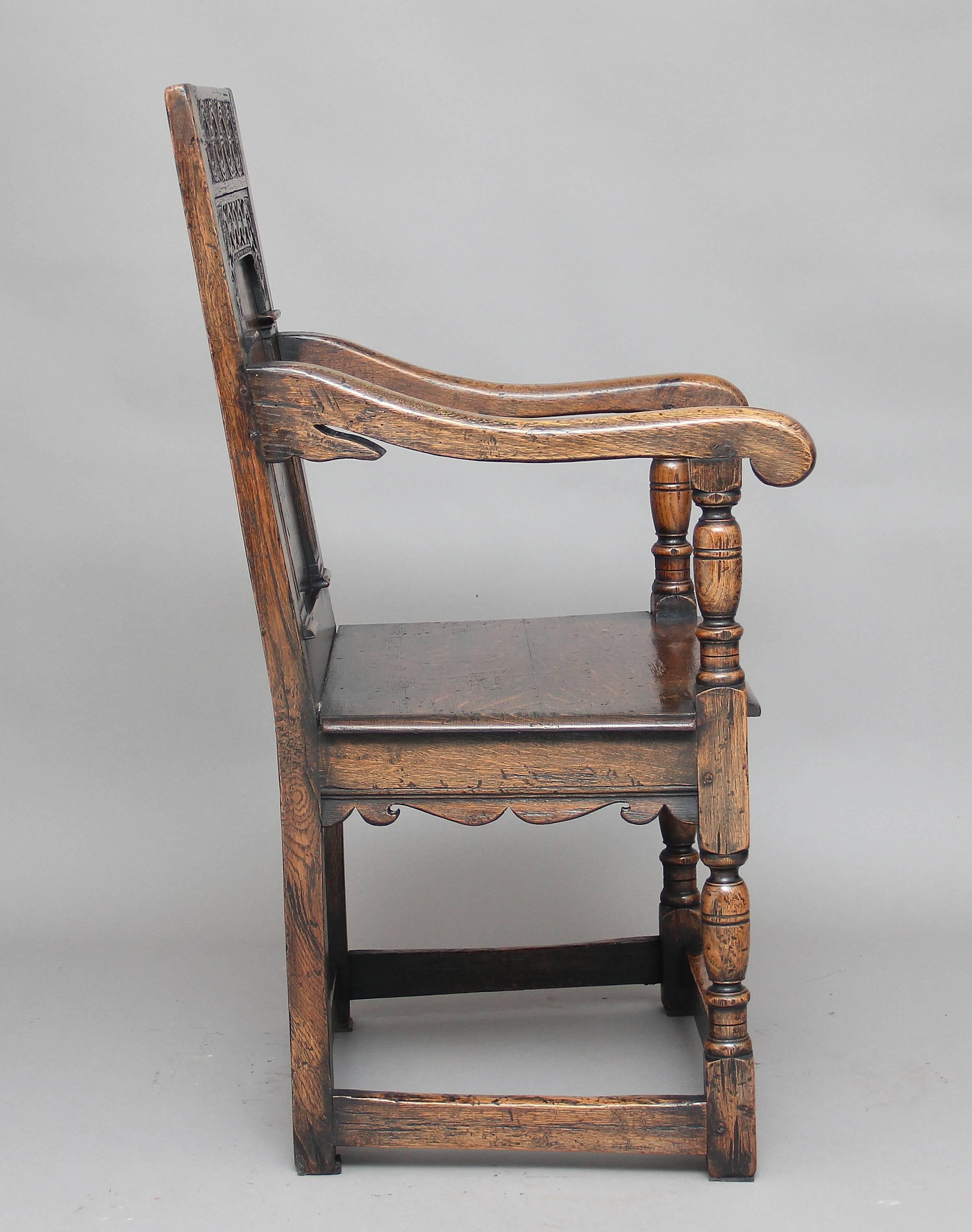 Early 20th century oak wainscot chair in the Tudor style, the back carved with the Tudor rose and a fluted and carved arch with a square and diamond marquetry inlay in the panel, the turned front legs holding nice swept bold arms, the legs united at