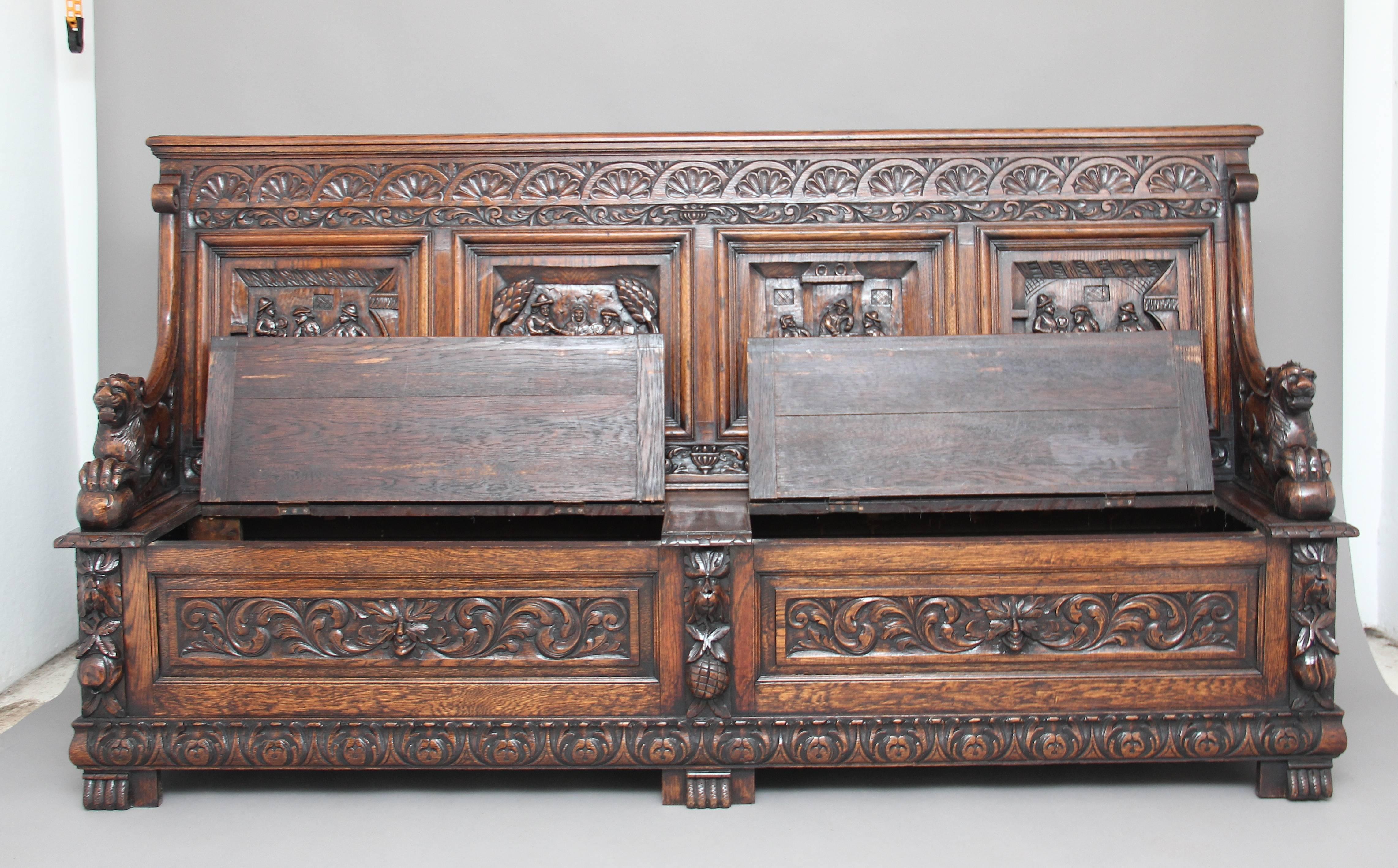 A superb quality large 19th century Flemish oak box settle that is very well carved, the back having four carved panels depicting tavern scenes, the arms carved with lions with their front paws on a ball, the seat with two lift up lids to reveal
