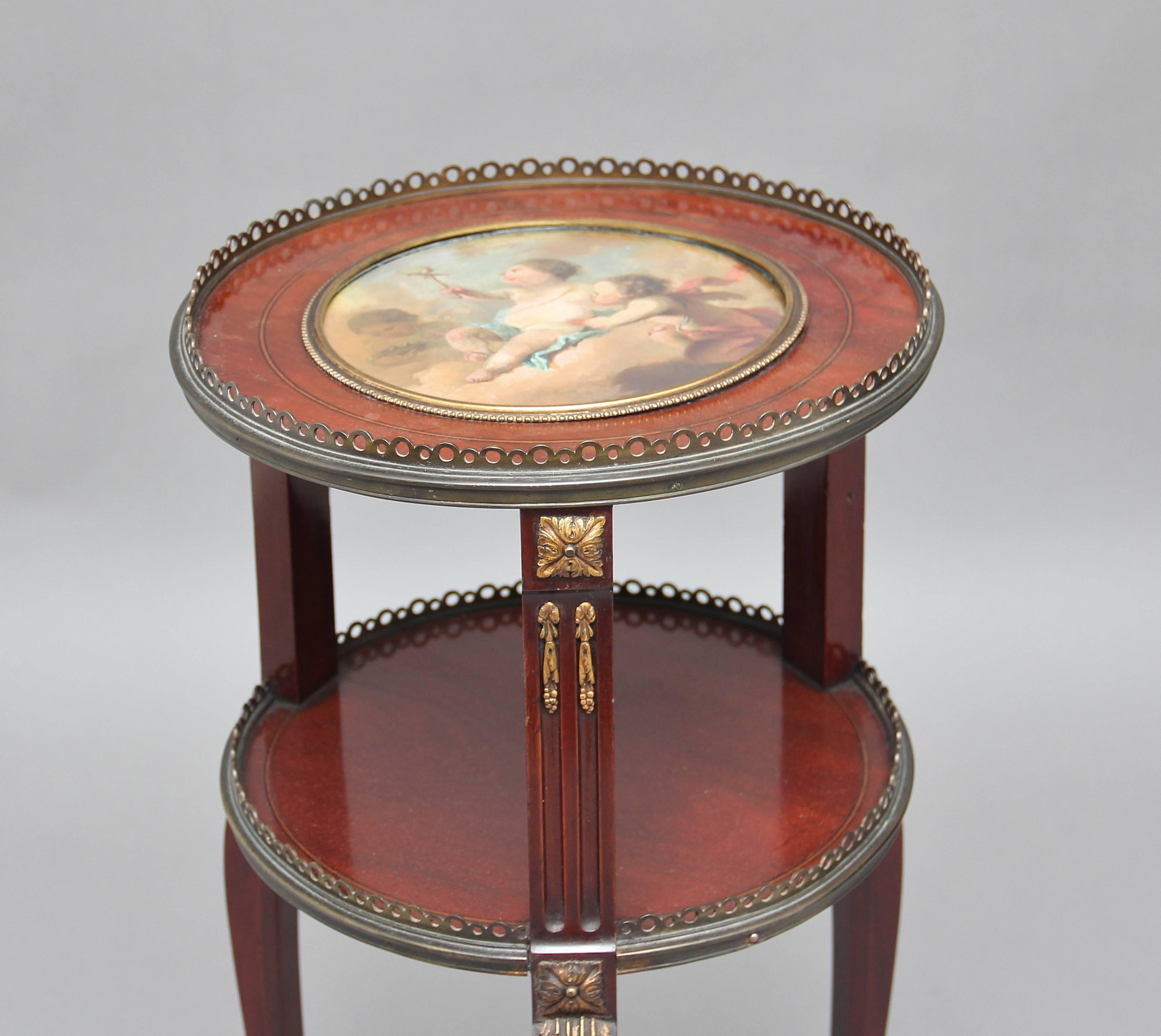 19th century French two-tier mahogany occasional table, the top having a brass gallery and a round section with a wonderfully painted picture under glass in the 18th century style depicting three cherubs, outside of the glass having a nice brass