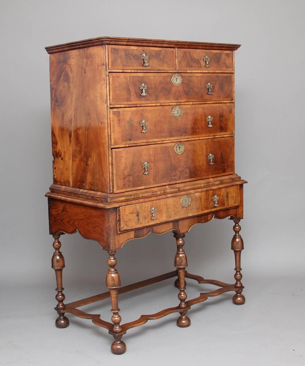 Early 18th century walnut and herring bone banded chest on stand, the chest having a stepped moulded cornice above a combination of two over four graduated long elm lined drawers, including a single drawer to the stand, with foliate embossed brass