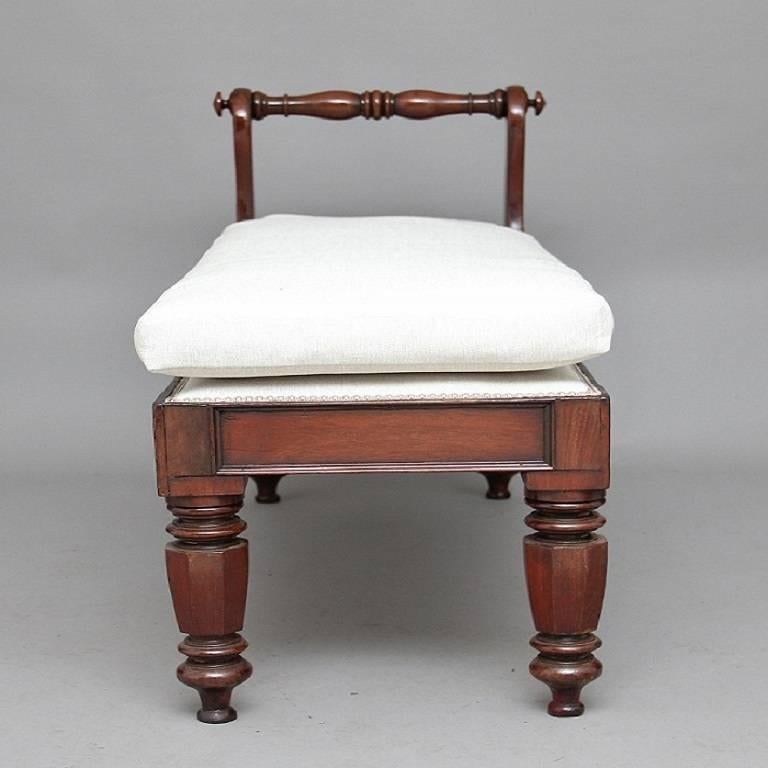 19th century mahogany window seat, the seat upholstered in a grey fabric with a grey upholstered cushion sitting on top, with turned baluster scroll ends, raised on octagonal section tapering supports, circa 1850.
 