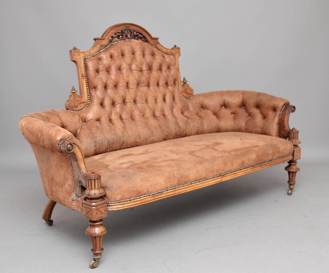 19th century walnut sofa in the art’s and craft style, the tub shaped sofa with buttoned brown leather upholstery with stud work decoration, the walnut frame comprising of various carving and finials, supported on turned and carved legs, circa 1870.