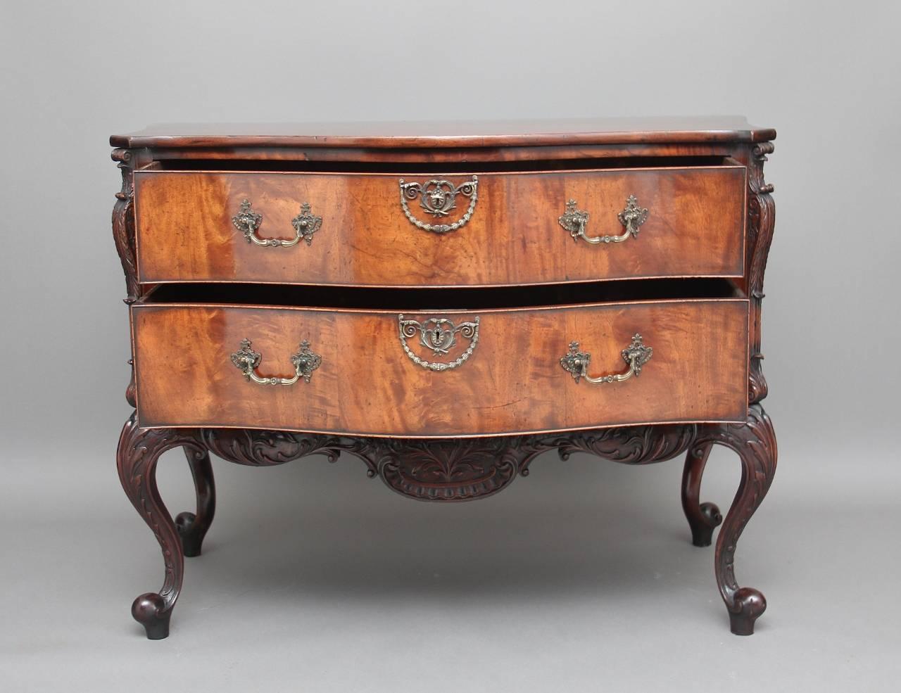 Early 20th century mahogany serpentine commode, the shaped oversailing top above two long graduated cockbeaded drawers, with original brass swan neck handles and escutcheons, the commode having a wonderfully carved and shaped apron, with scrolling