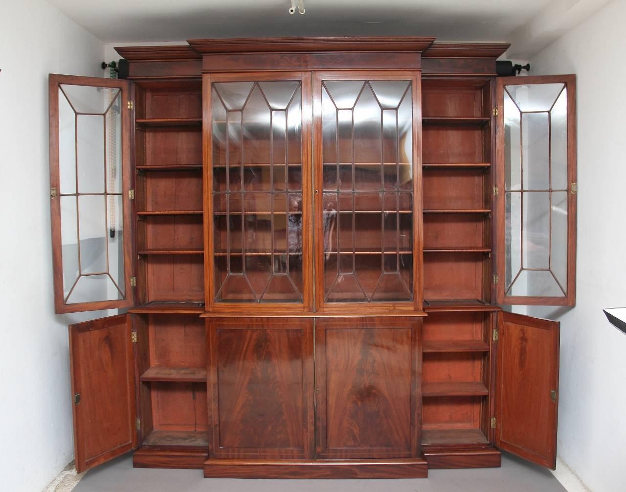 19th century four door mahogany breakfront bookcase, the moulded cornice above four astragal glazed doors opening to reveal four adjustable shelves in each section, the bottom section having four cupboards with flame mahogany panel doors, the