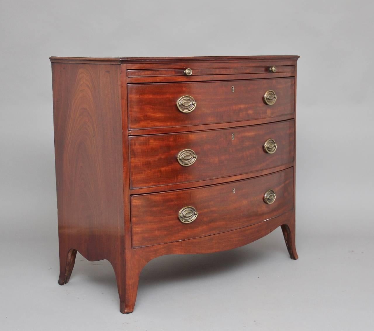 Early 19th century mahogany bowfront chest of drawers, the moulded edge top having a brushing slide below and three graduated oak lined drawers with oval brass handles, with a shaped apron along the sides and front standing on splay feet, circa 1800.