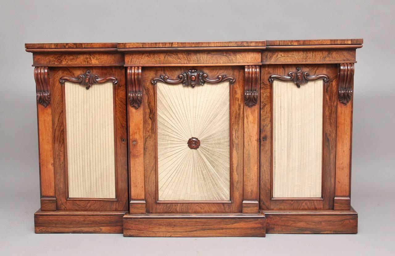19th century rosewood breakfront cabinet with three doors with silk panels, each door opening to reveal two adjustable shelves, the front of the bookcase having some lovely crisply carved decoration, standing on a plinth base, circa 1830.
 
