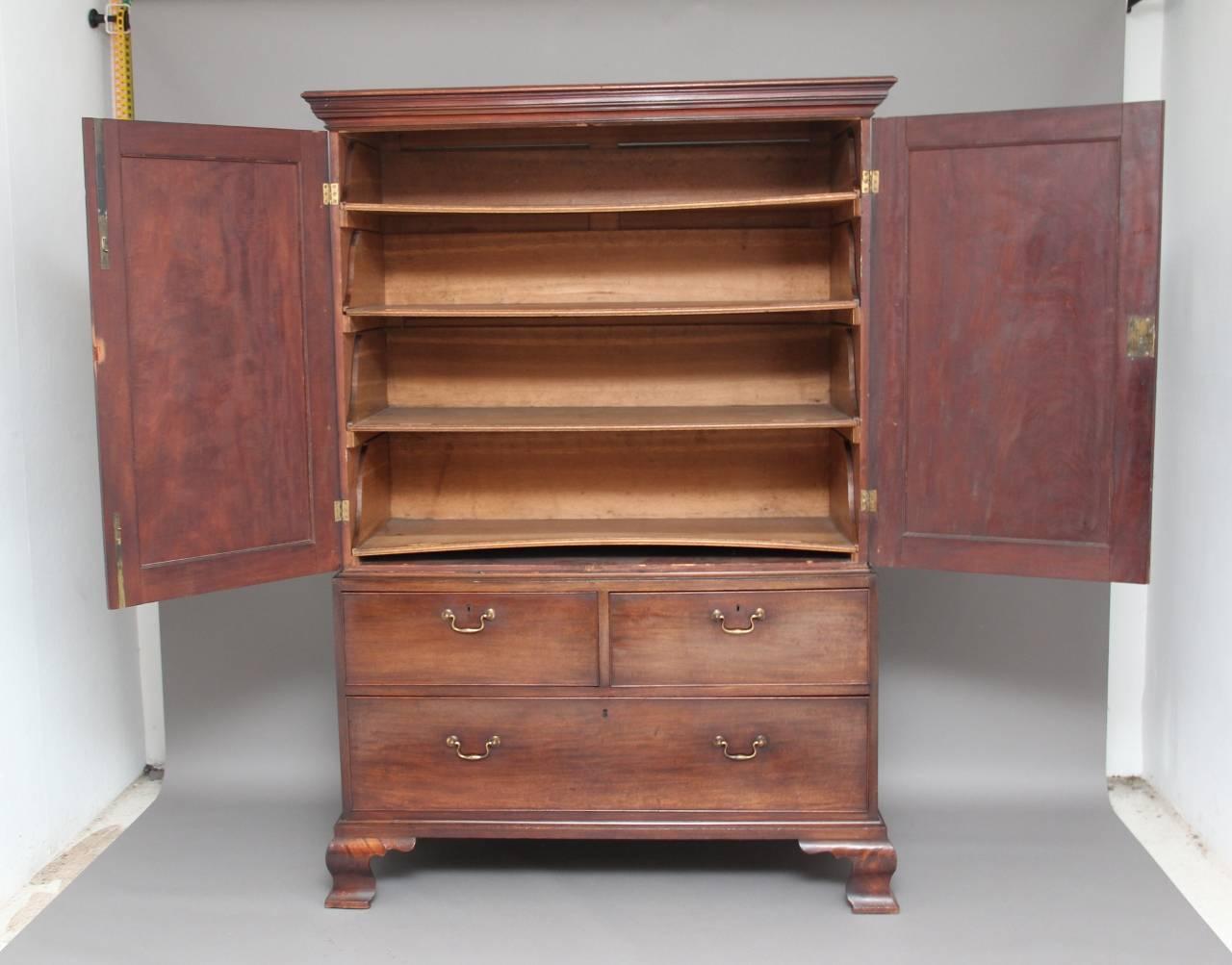 18th century mahogany press cupboard, with a stepped moulded cornice and a two-door cupboard below, the doors with moulded panels with carved decoration in the corners, opening to reveal four original oak trays, the bottom section having two large