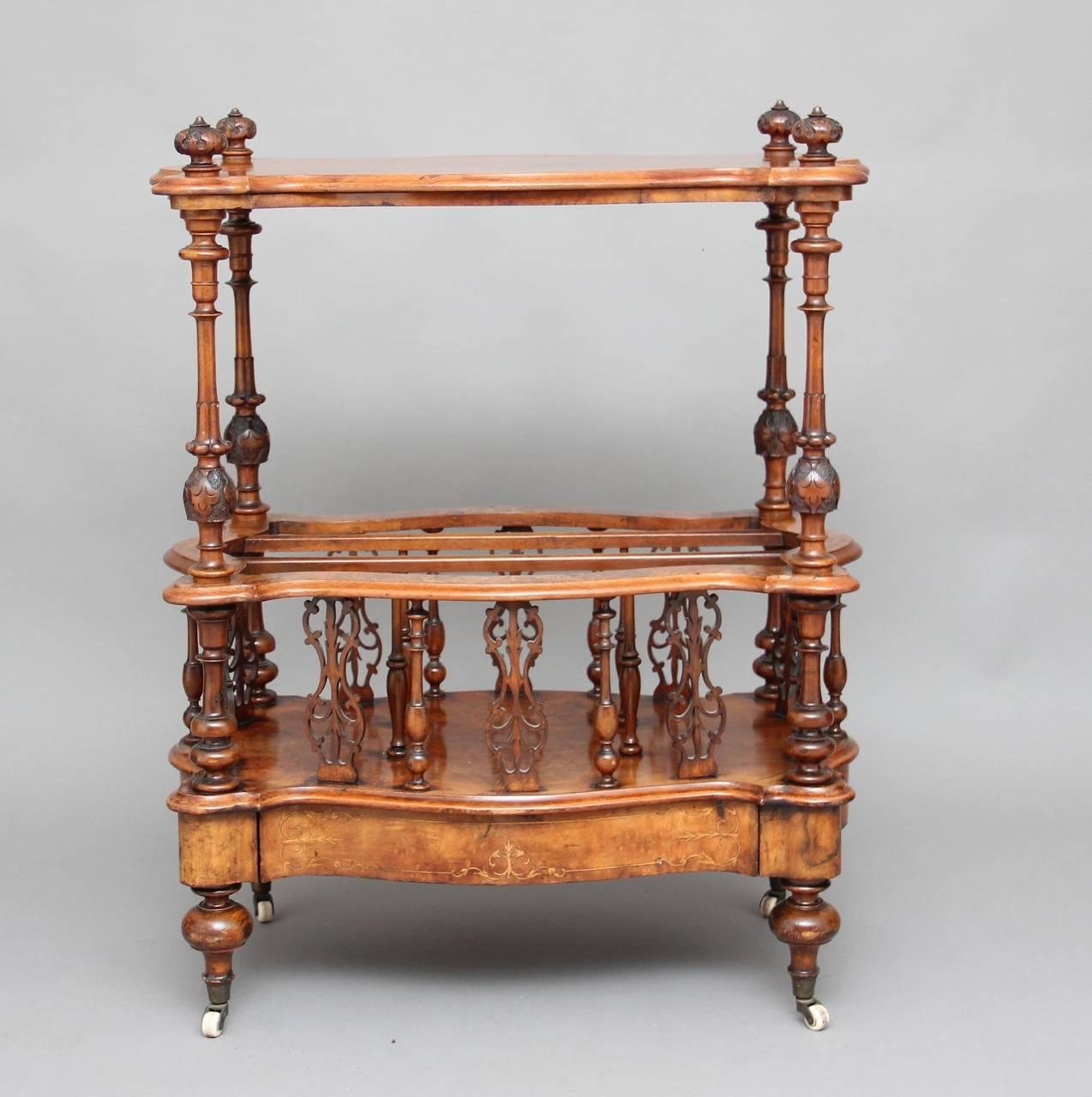 19th century serpentine shaped burr walnut Canterbury, the shaped top decorated with fine inlay and having carved finials in each corner, supported on four carved and turned columns, the middle section having three divisions which is divided by