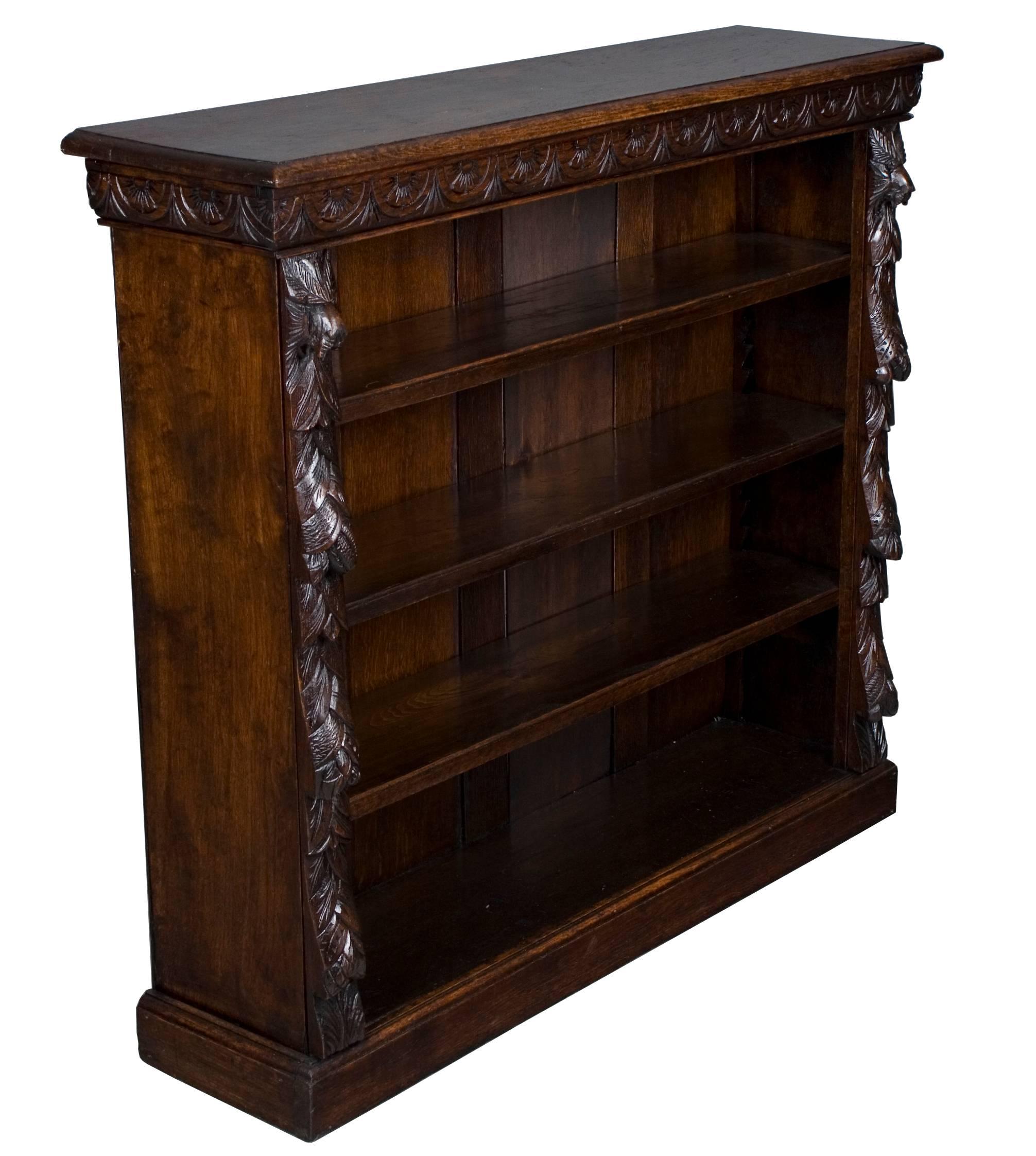 This beautiful short bookcase was made in England around the year 1890. Done in a stunning carved oak, it has a very dark color. Typical for the period, the sides have a green mask carving at the top with flora flowing down below and half circles