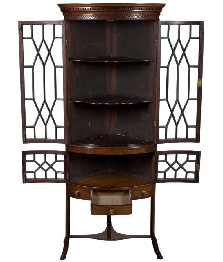 This mahogany bow front corner cabinet on legs comes from England where it was made around 1940. The unique look of the delicate legs combined with the old style wavy glass of the doors makes this quite an exciting piece. Four glass doors in total