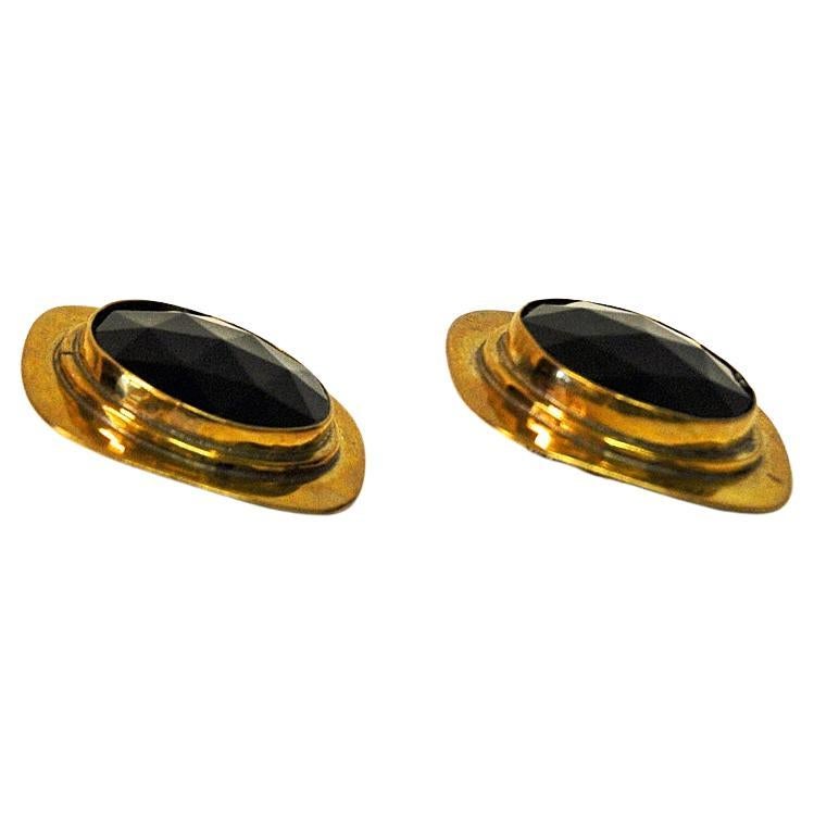 Midcentury brass clip earrings with a dark purple glass stone in the middle with a cut rock shape. Designed by Anna Greta Eker, Norway, 1960s. A typical couple of vintage earrings reflecting some of the best work within design and silversmith art by