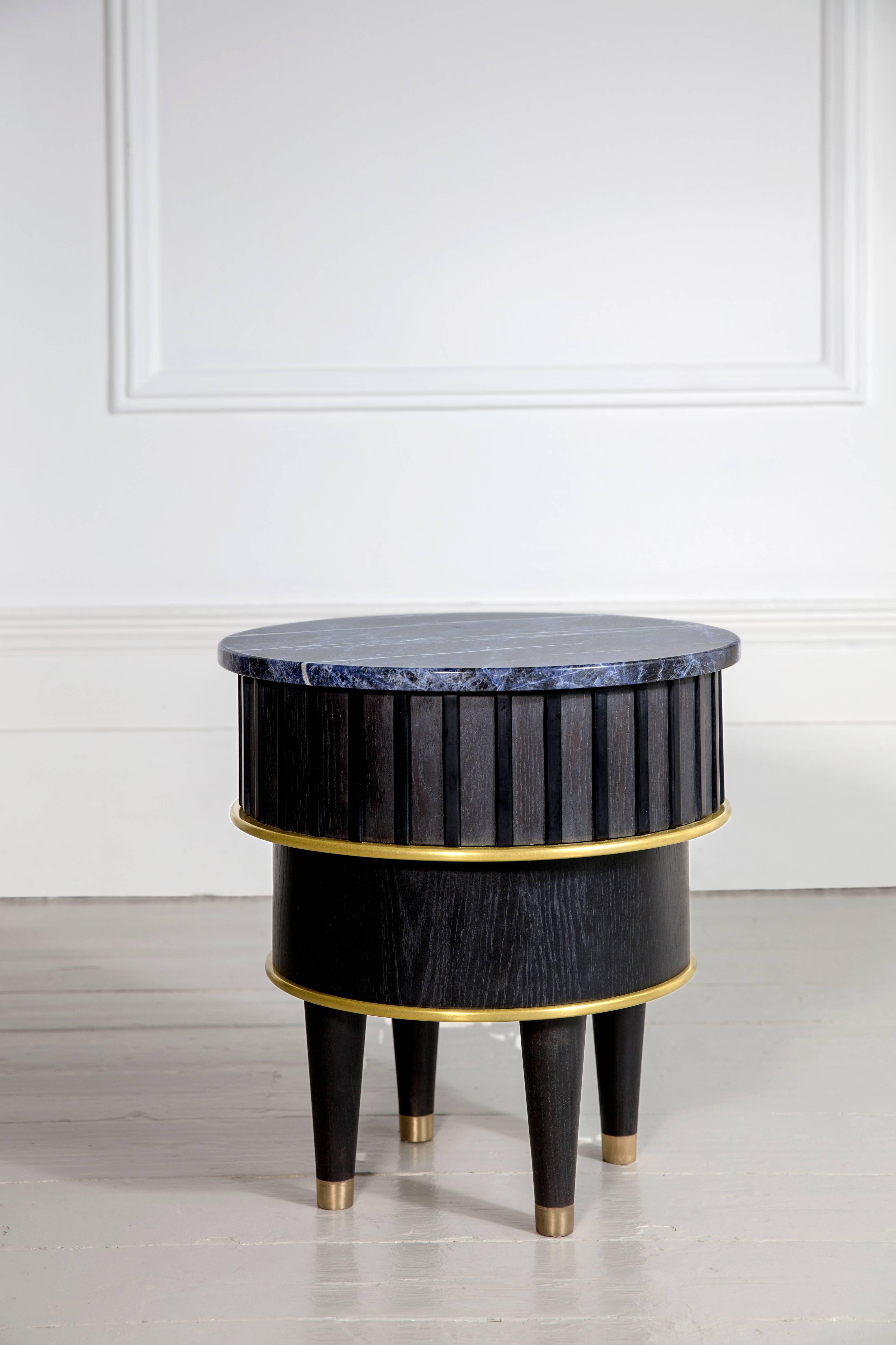 A beautiful Corian and sodalite top paired with blackened oak and liquid brass. This blackened oak table includes solid brass socks. Black Corian and liquid brass accents, crowned with a semi precious sodalite stone top.
This side table evokes a
