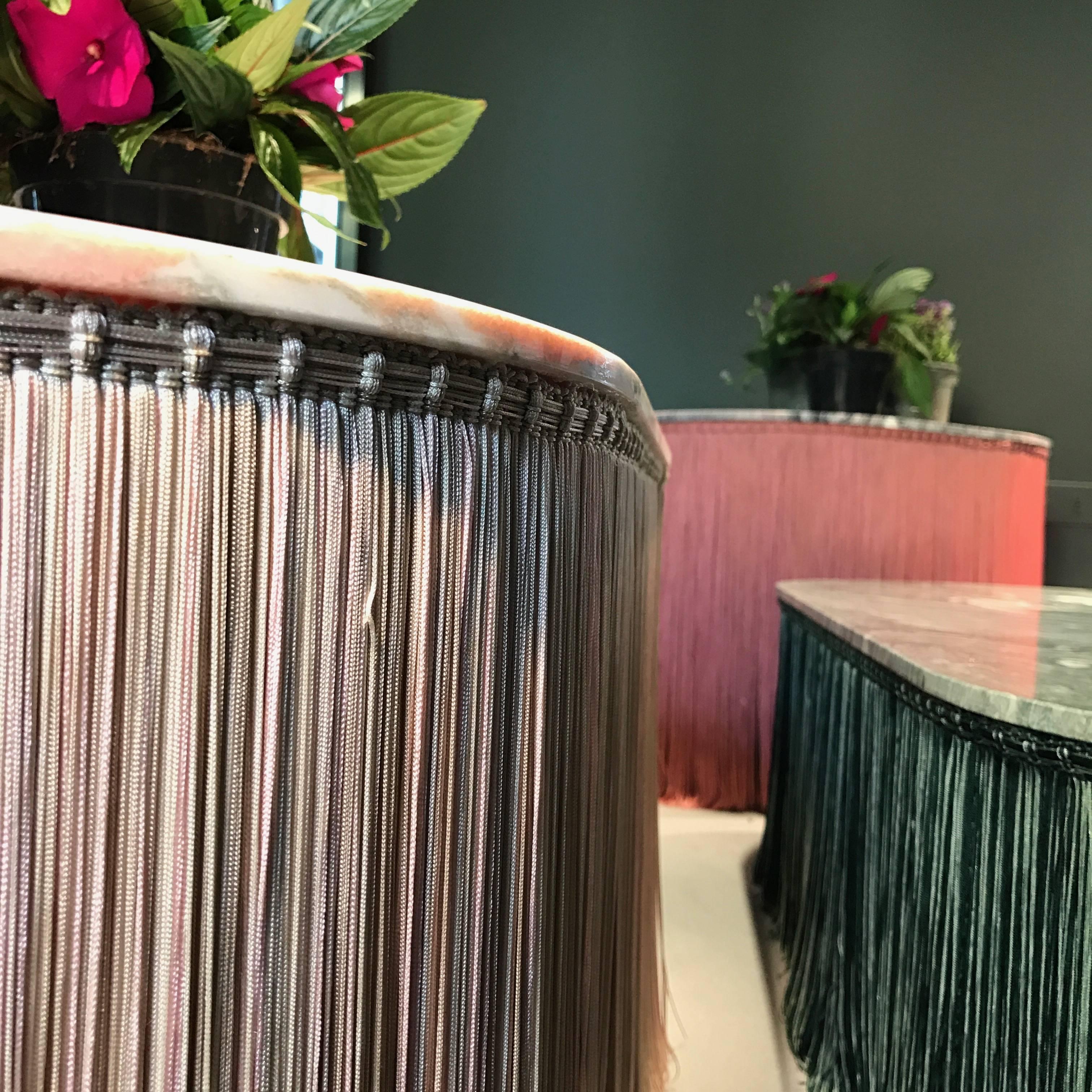 Low table in Pink Norvegia marble and coordinated fringes. 
Tripolino plays with the iconic element of passementerie usually used as a decorative element of bourgeois lounges.
Applied to the edges of the table, it looks as fringes are sustaining its