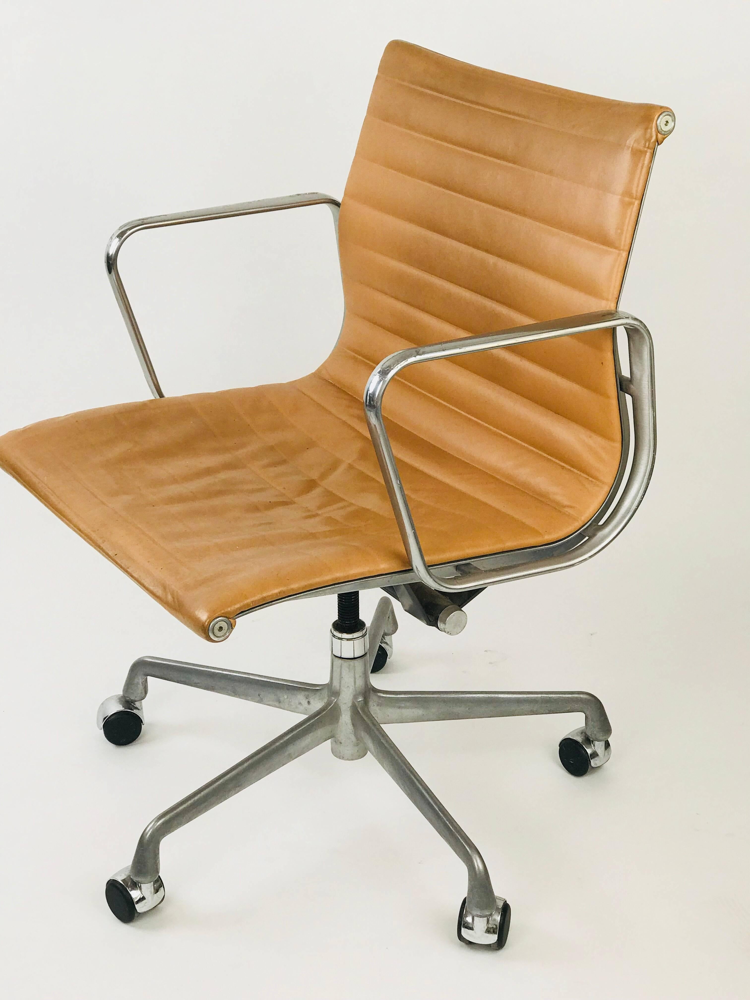 Eames management office chair designed by Charles Eames for Herman Miller in camel leather. Has a five-star base, spindle and tilt-swivel mechanism. It is in fair condition with some minor damage to the metal on the arms and a worn seat that adds to