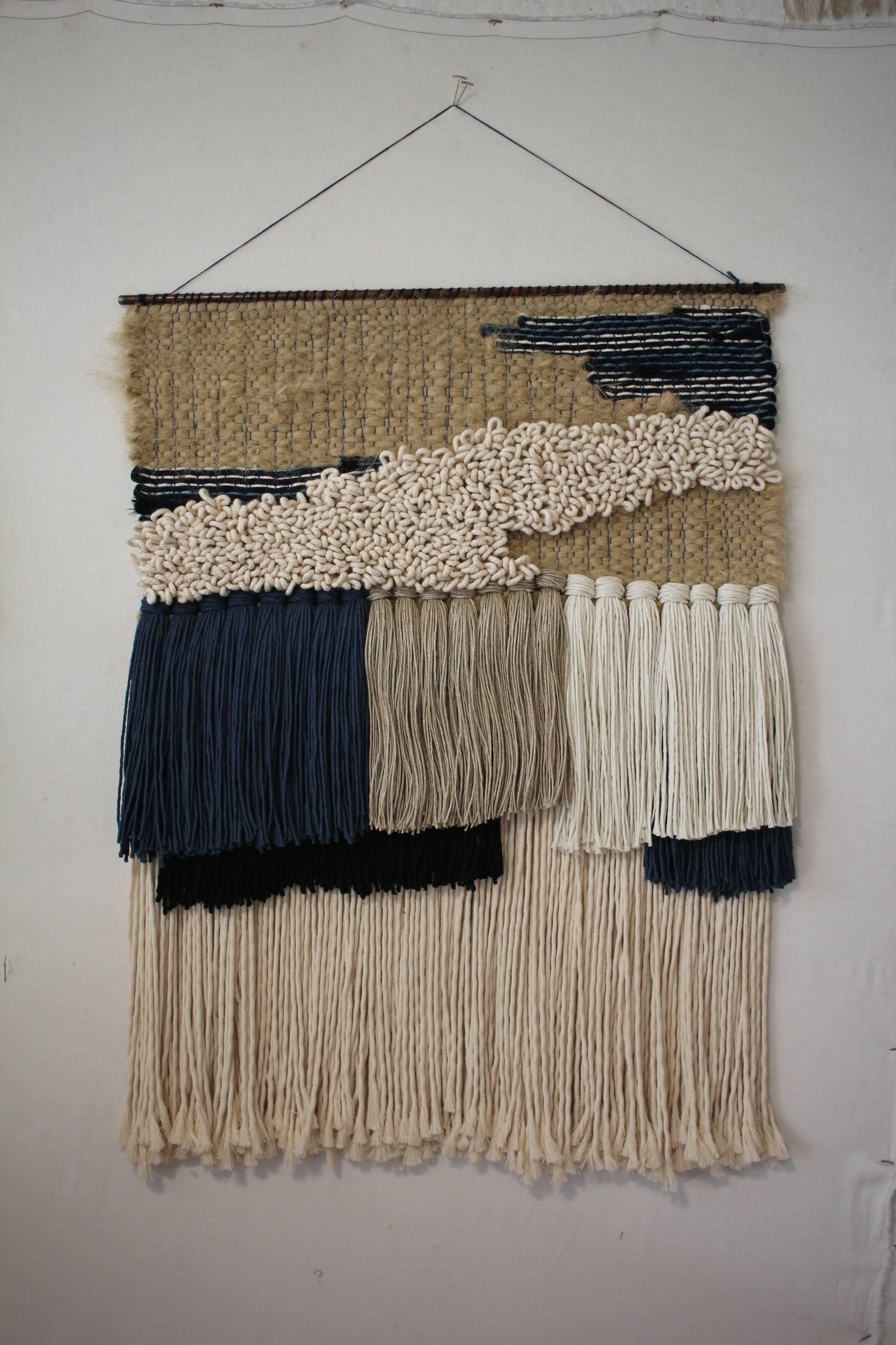 Handwoven, tapestry style, wall hanging by Janelle Pietrzak of All Roads. Colors are natural hemp, natural undyed cotton, indigo and blue. Fibers used are cotton, hemp and merino wool. Weaving hangs from a round steel bar with a hanging string.