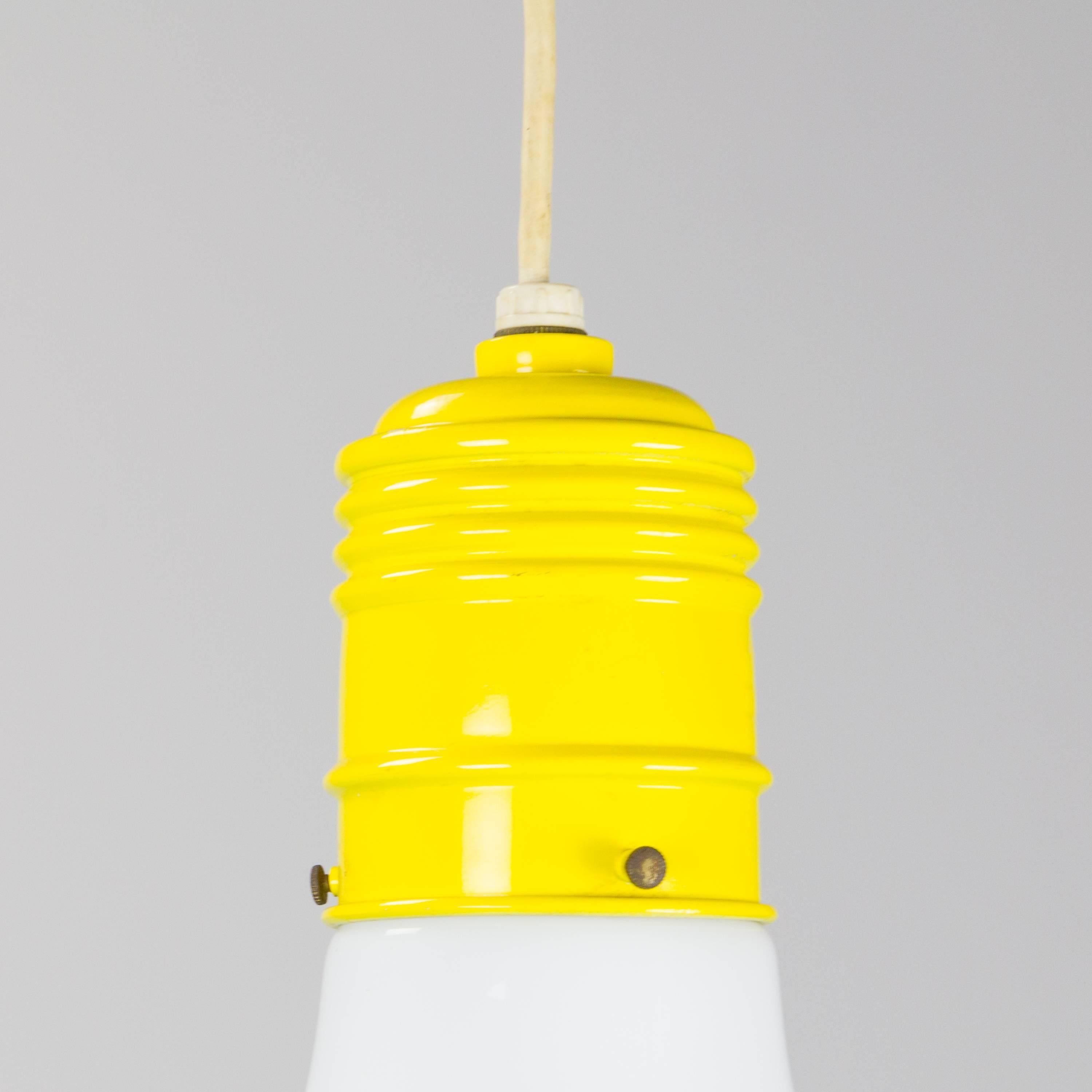 Oversized bulb pendant lamp by Ingo Maurer for Design M with opal glass bulb-form shade and yellow enameled metal socket. The lamp hangs from its cord and adjusts with two painted yellow wood cable-keeps.