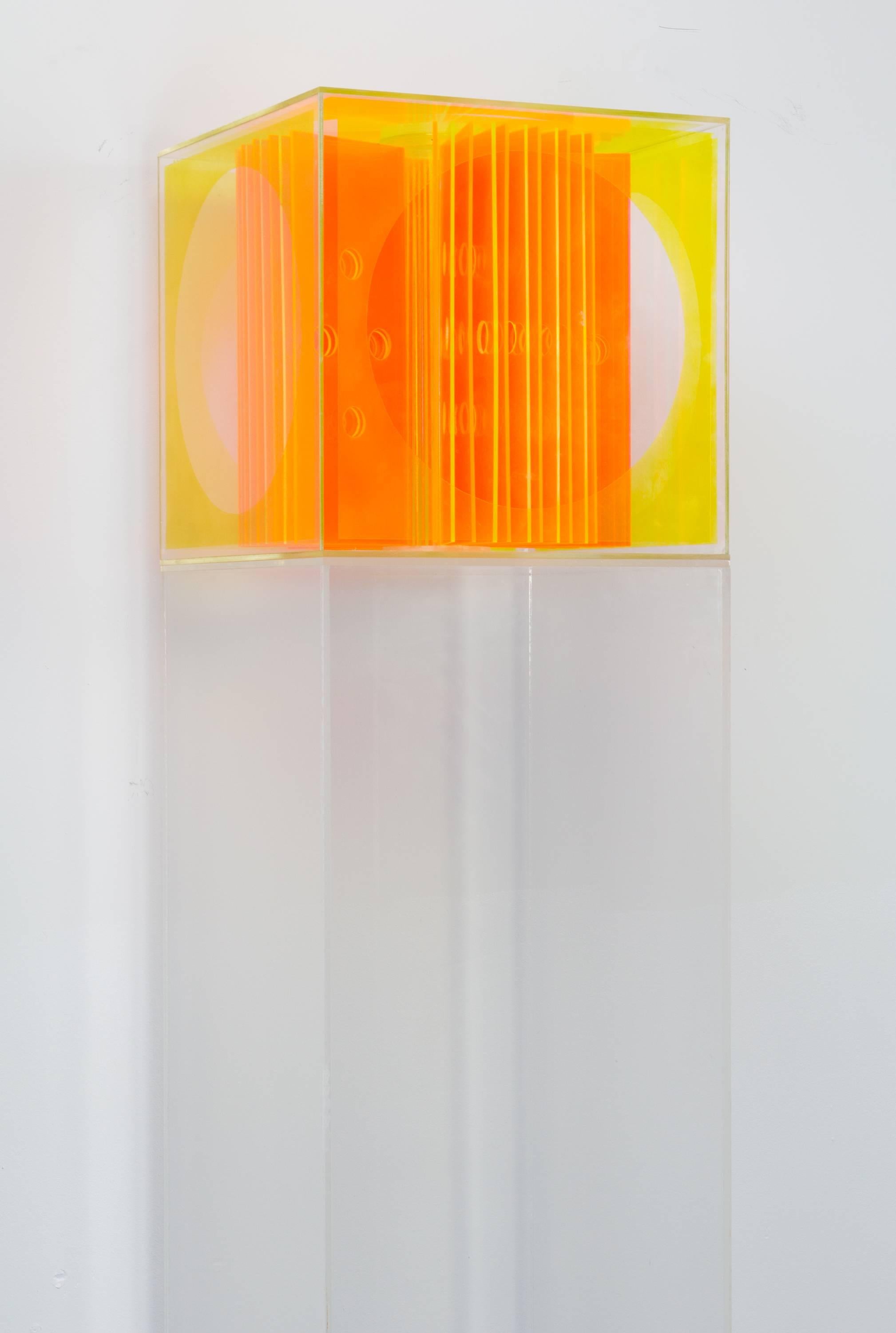 Bright acrylic Op-Art cube sculpture with perforated orange panels and yellow walls, set atop an acrylic pedestal.