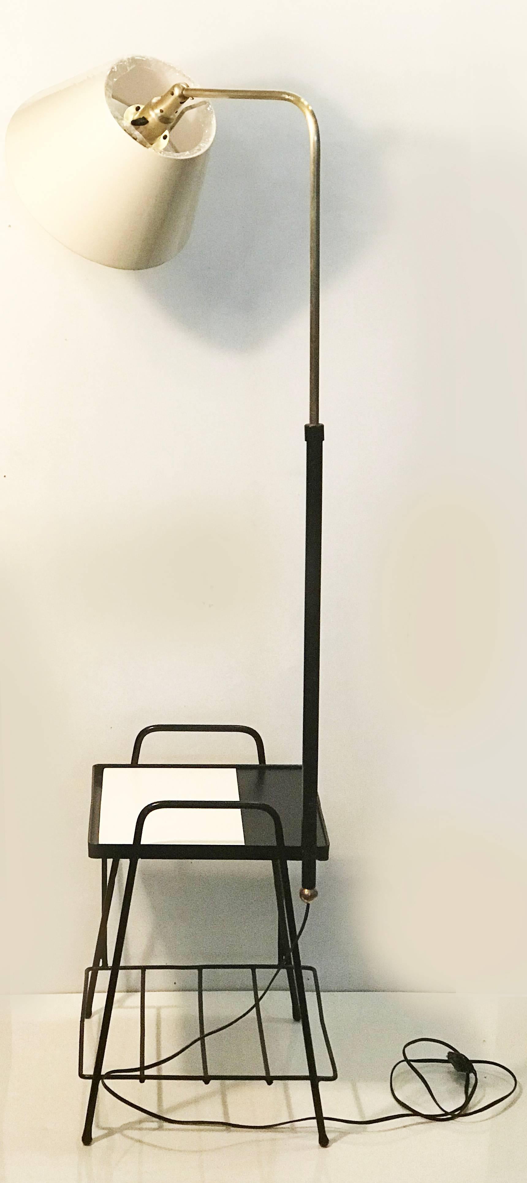This floor lamp features a square table (31 cm x 31 cm), a magazine rak and a shelve under the table, it has four iron legs ending in little round balls. The central arm that holds the shade, is extensible and made of brass, this arm also rotates