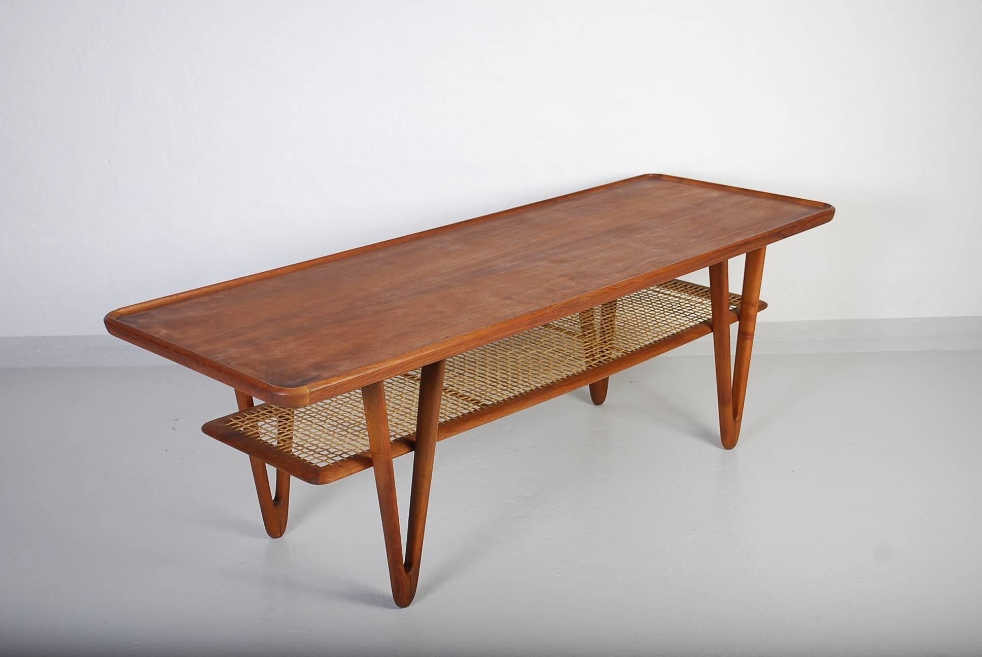 Midcentury solid teak coffee table by Danish designer Kurt Østervig. The coffee table has V-shaped legs and a cane shelf. The table is in very good vintage condition with minor signs of usage consistent with age and use.

This item will be available