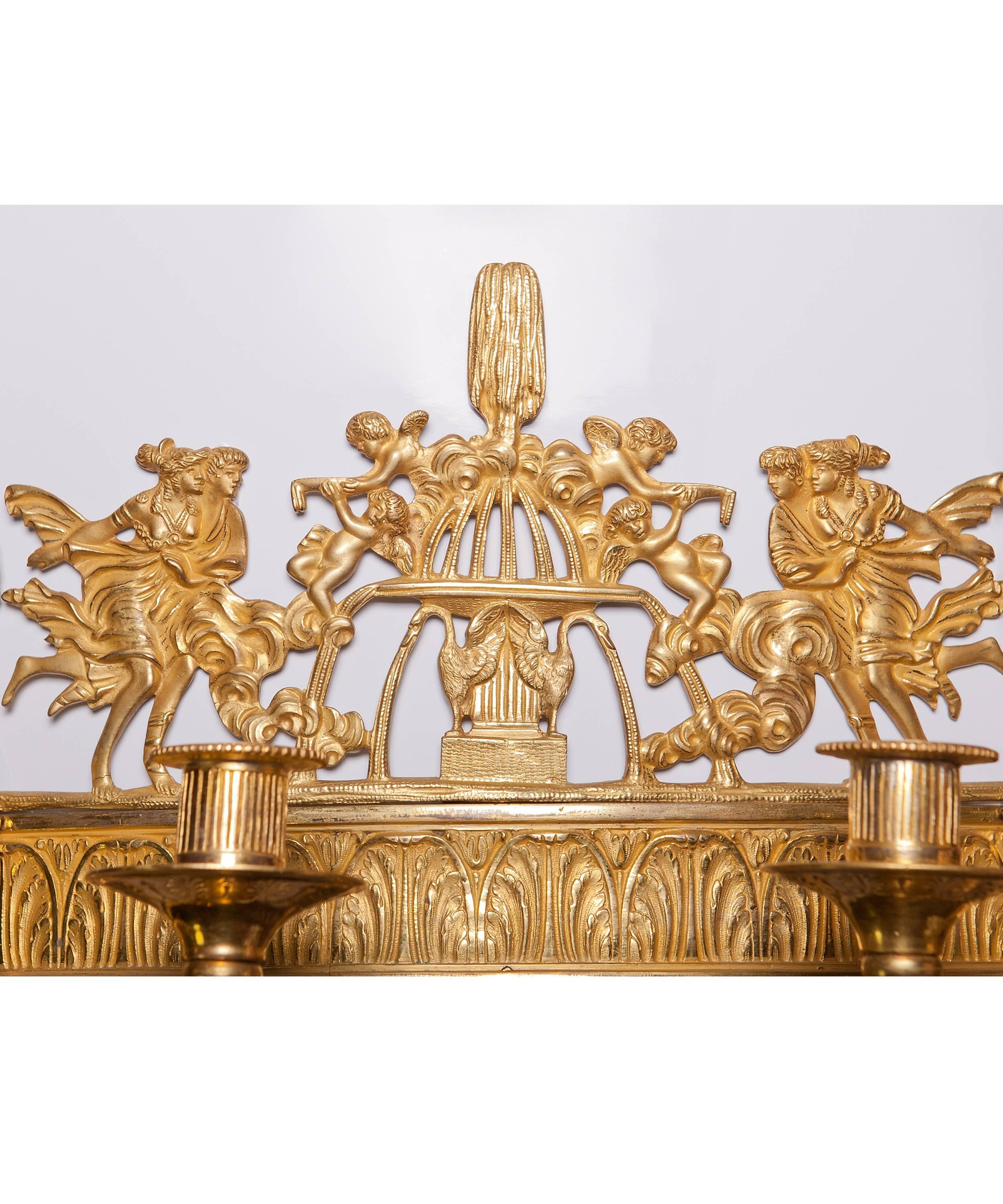 The eighteen-light chandelier is crowned with a gilded fire plateau decorated with 12 palm leaves and a pine-cone, from which large chains are leaving downwards to the centre ring. On this ring six three-light arms are decorated with the head of