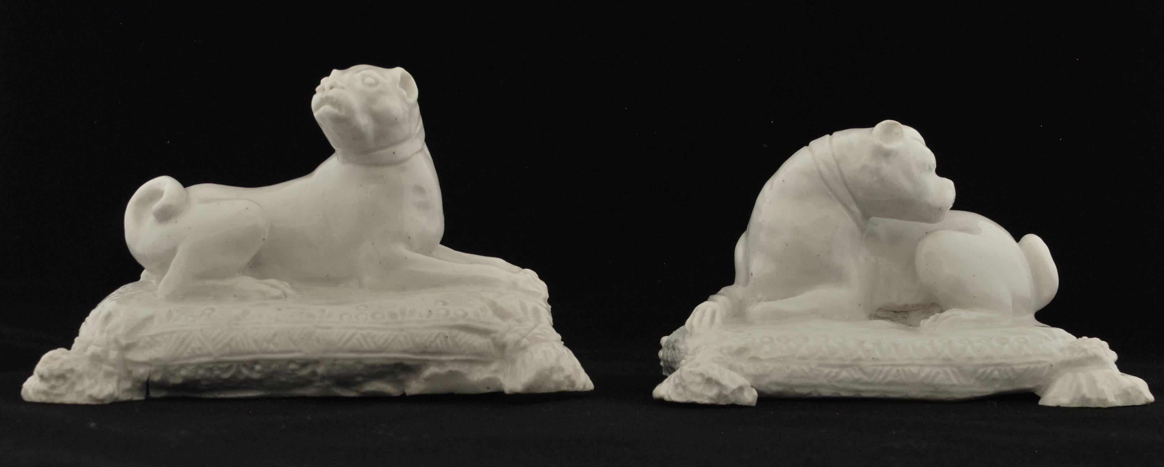 In the white. Each recumbent on an integrated base moulded as a cushion with ‘embroidered’ edge and tasselled corners; the bitch with head raised, the dog sleeping with head turned, each with a wide collar. Porcelain of deep cream colour and even