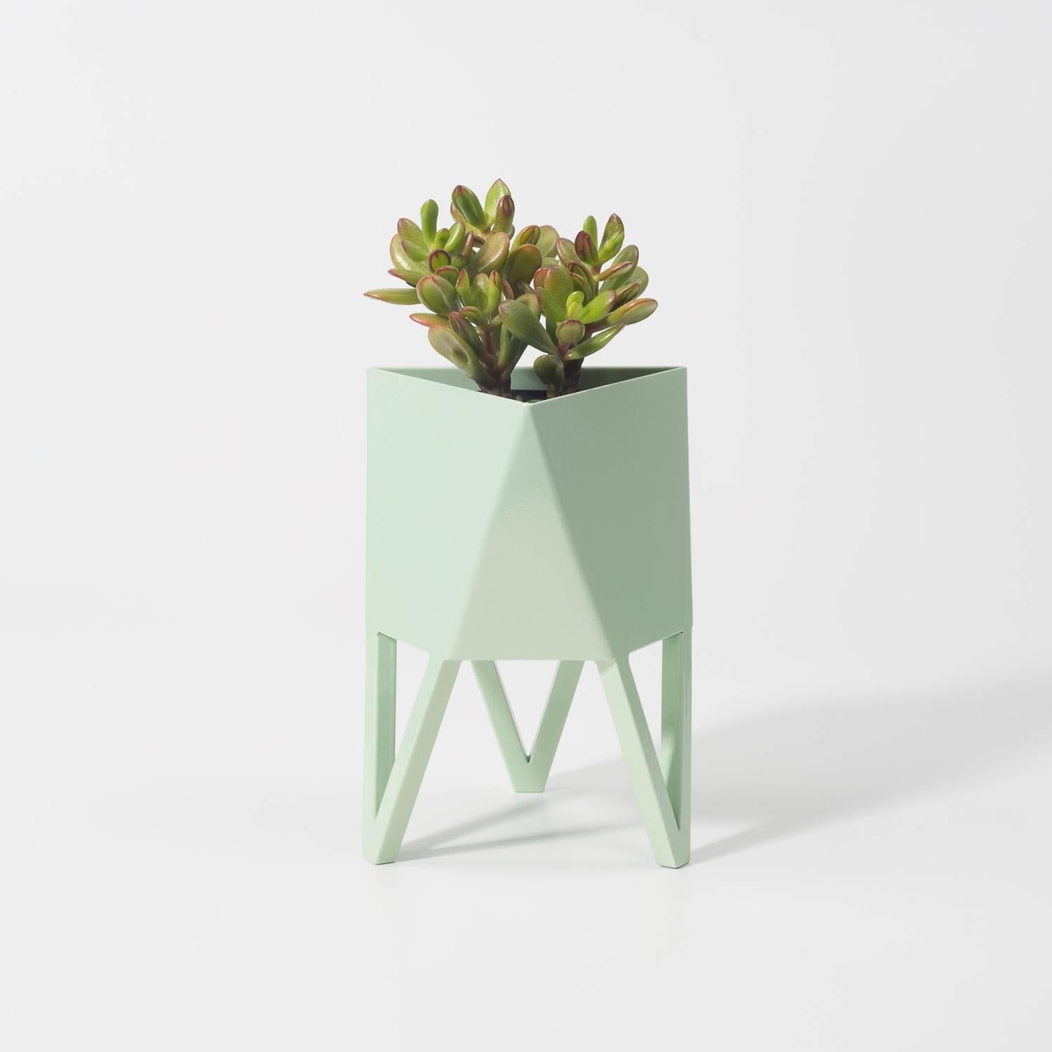 Introducing Force/Collide's signature planter in flat pastel green. Using a seamless brake-forming technique, one sheet of steel is wrapped into a unique geometric pattern that's triangular at the top and hexagonal at the base. Three V-shaped legs