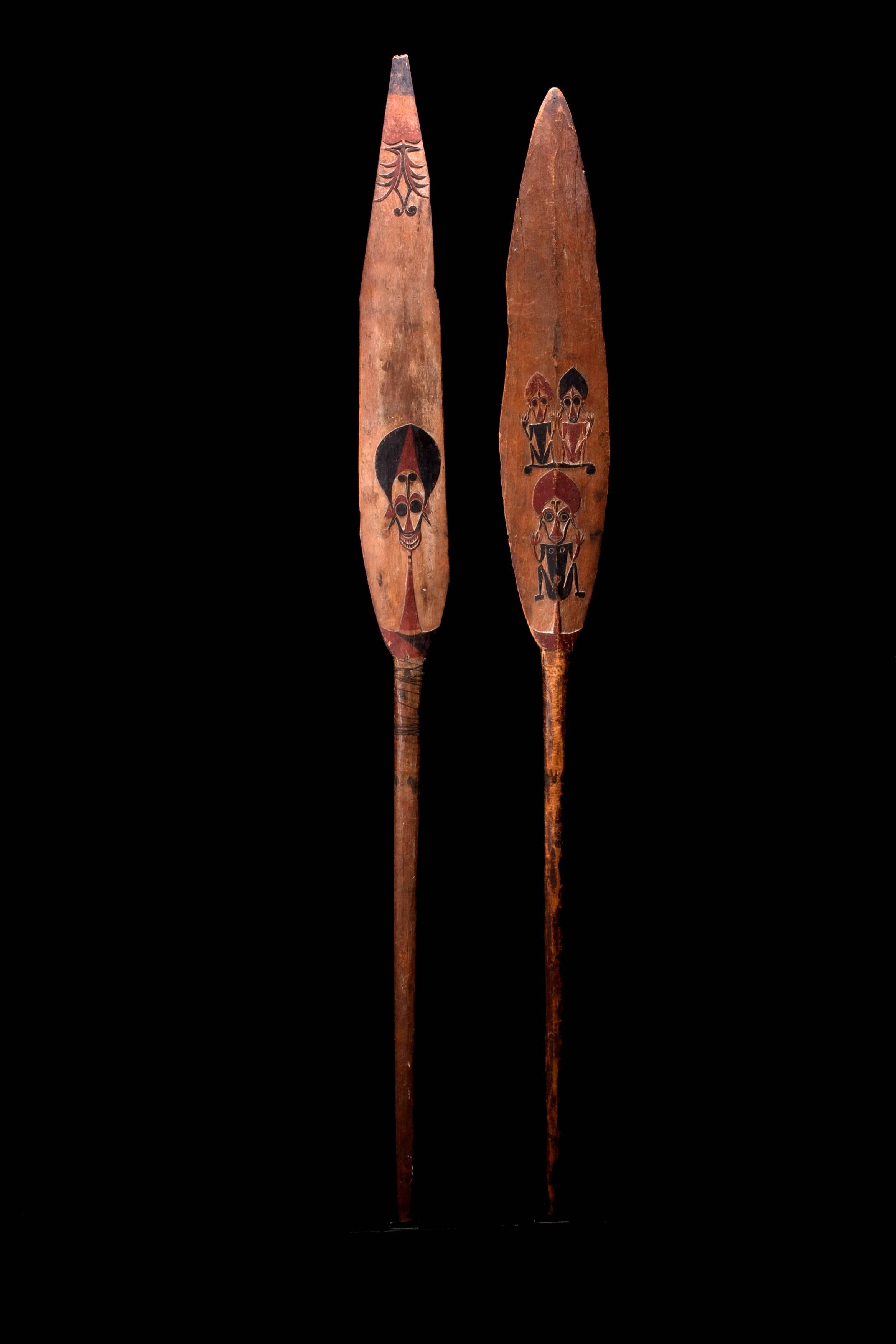 Two paddles with flat, long, lentoid blades and central raised ridges, with long handles or flattened ovoid form. The shorter paddle is adorned with three relief squatting “Kokorra”, the powerful iconic spirits associated with the men’s secret