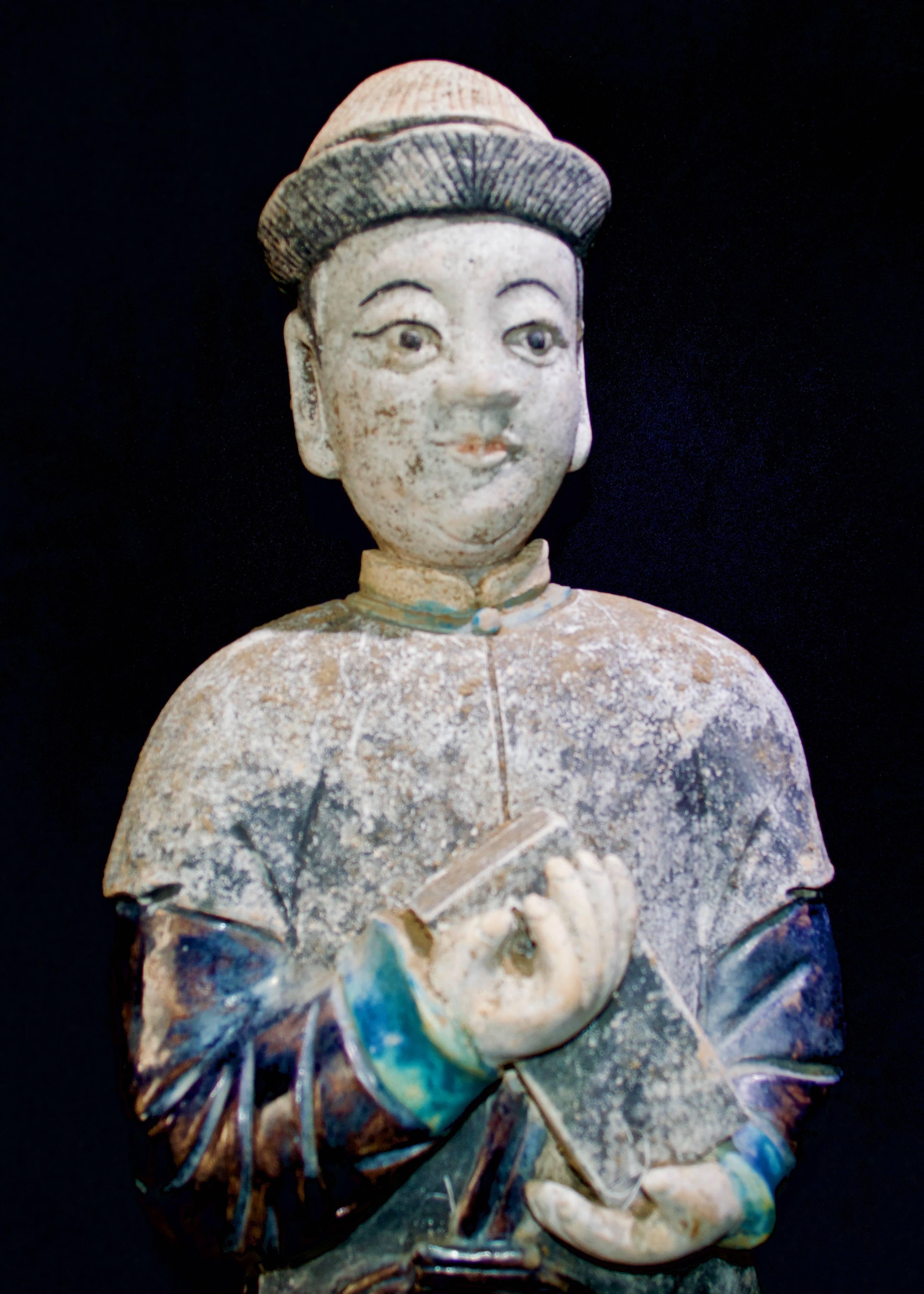 A magnificent male courtier from the Ming dynasty, 1368-1644 AD, in excellent condition. At 82 cm tall, this immense figure is wearing a traditional hanfu shades of blue and black. It is standing on a rectangular black & blue plinth and the unglazed