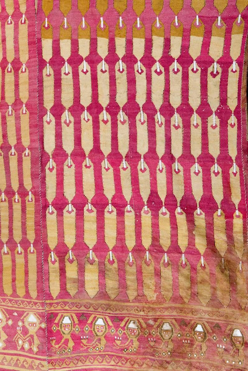 An intact shirt with motif of rows of feathers in several shades of mustard yellow on a red ground, depicted as they would have been attached in rows in an actual feather textile.