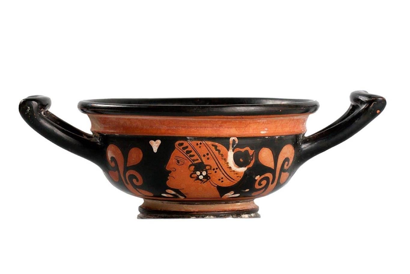 A low pottery cup on ring base with deep bowl type body and two graceful, squared handles extending at opposing sides. Exterior with red-figure painted reclining figure, probably Dionysus holding a bowl. The bearded figure wears a draped garment on