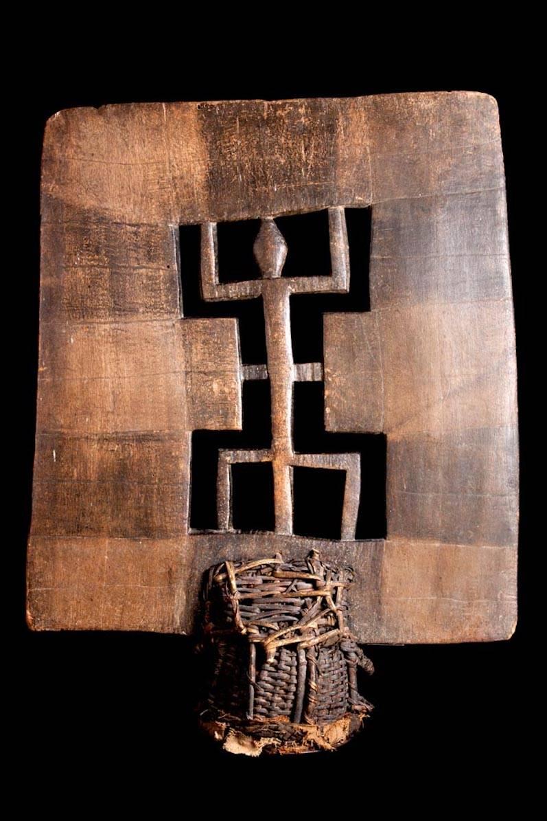 Large openwork crest mounted upon a woven basketry cap. The large, square decorative panel bears a central reptilian or stylized crocodile depiction with alternating squared painted brown and the natural tan wood color. Some chipping and wear. Cloth