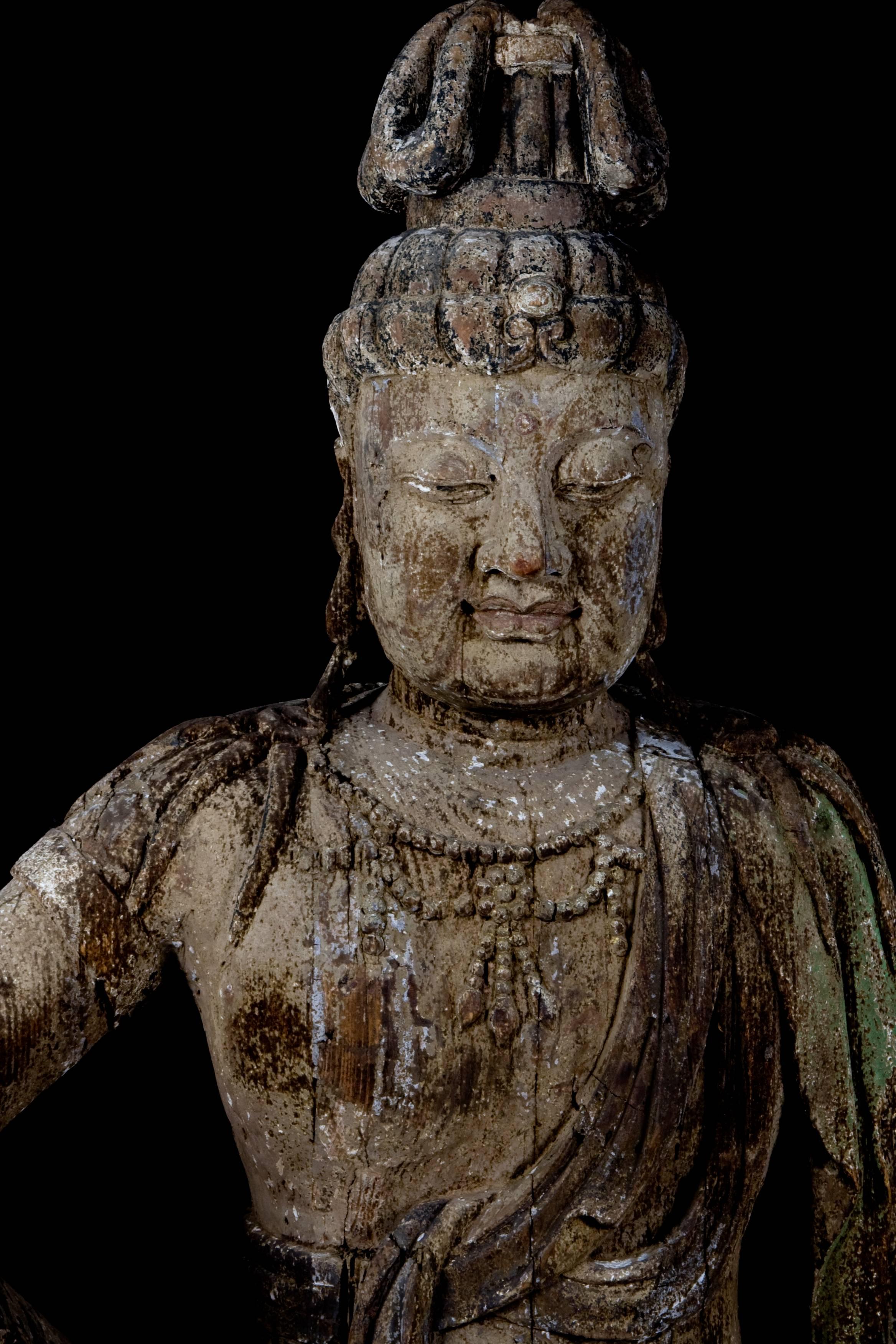 Imposante Bodhisattva-Figur in königlicher Pose mit schönem, heiterem Ausdruck, mit halbgeschlossenen Augen, die Glückseligkeit ausdrücken, in sehr gut geschnitzten Gewändern und Perlenschnüren an Hals und Knien. Spuren der ursprünglichen