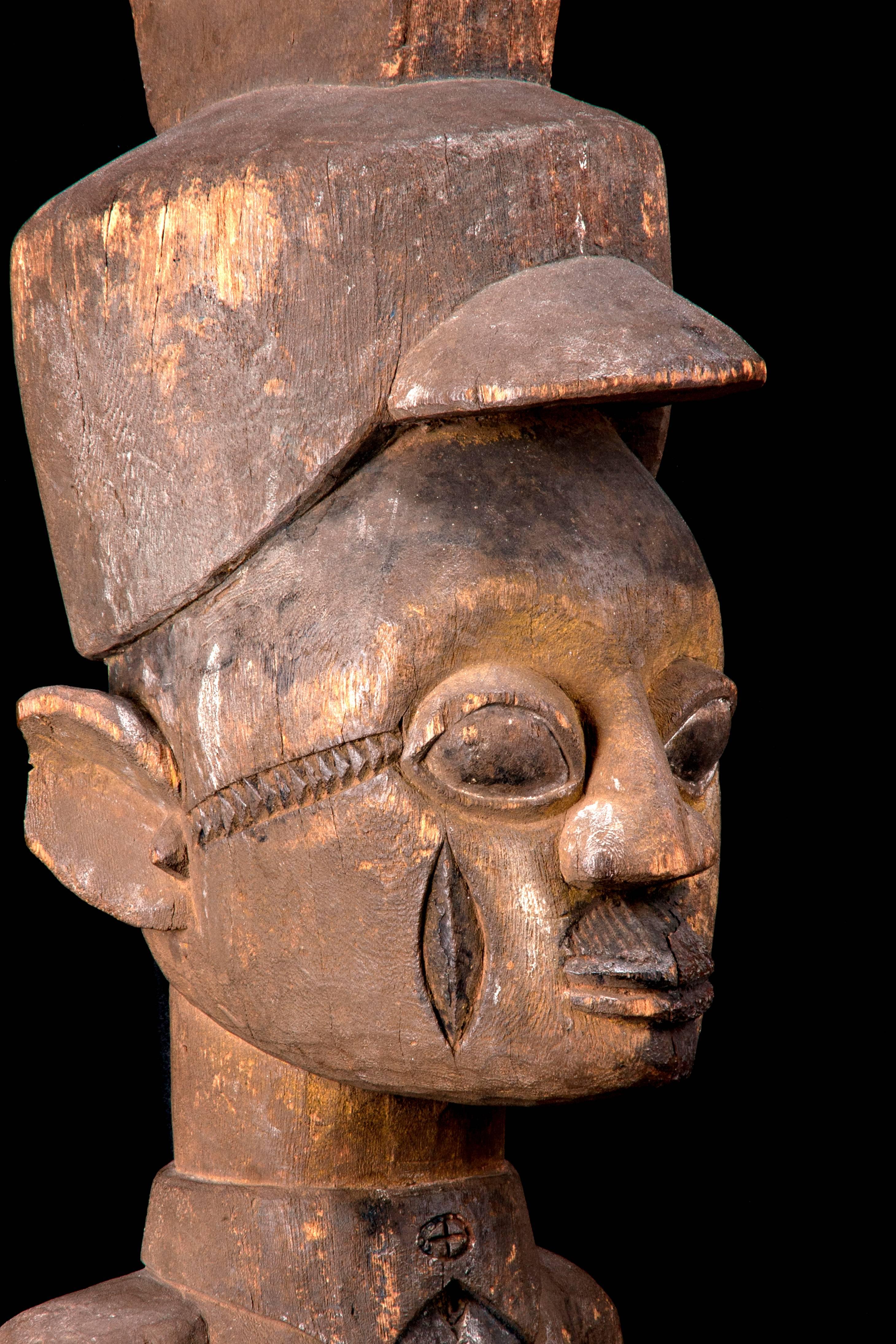 A European functionary, a cane in his right hand, carries a ledger in his left, he wears a visored CAP, collar and tie. He is moustached and has a cigar in his jacket pocket.  Probably carved by Ayantola of Odo-Ehin near Efon-Alaye, flourished about