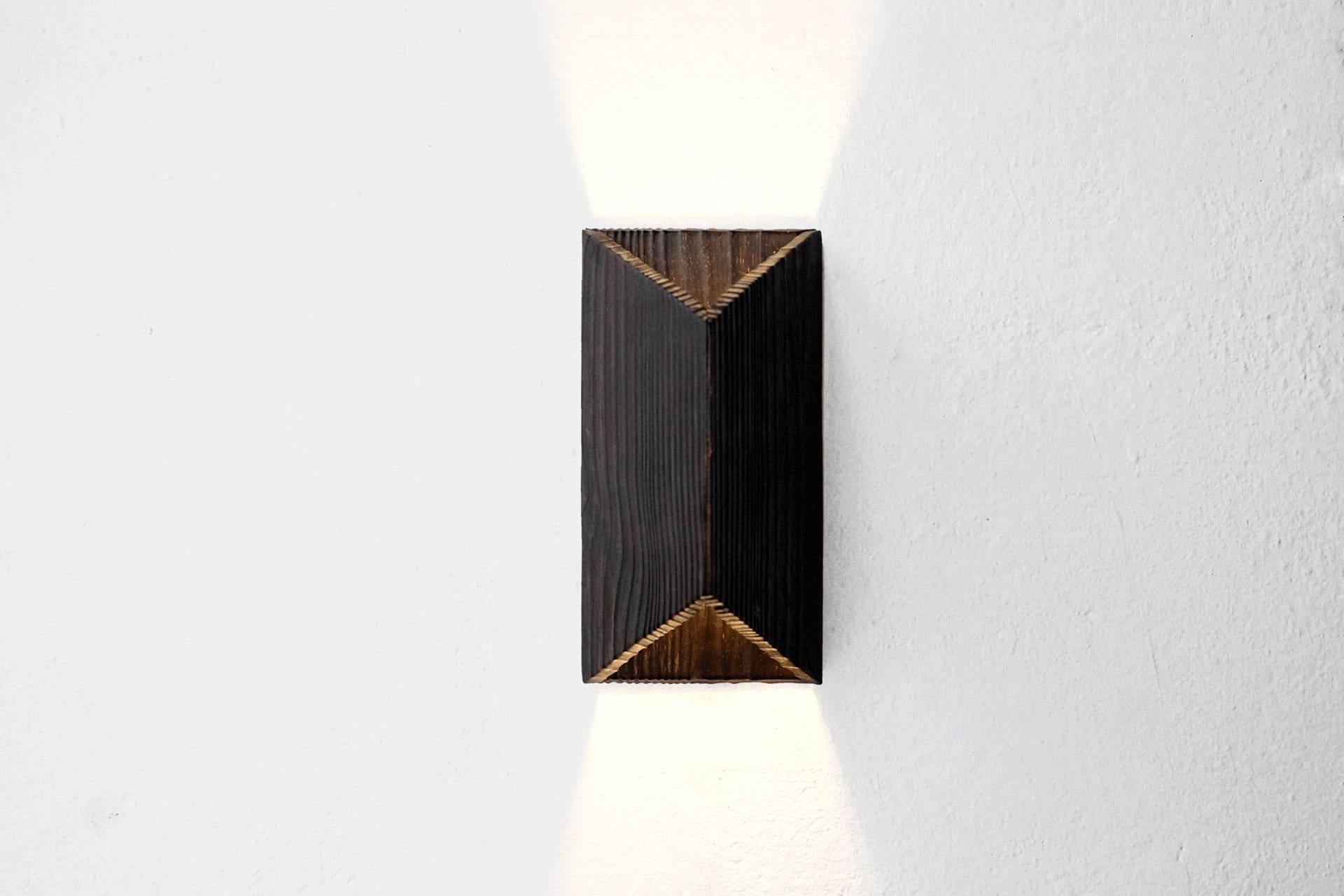 This wall lamp or sconce integrates into the Nuno lamp family, which finishing treatment was inspired by Shou sugi ban or Yakisugi, a Japanese ancient technique of wood burning, used in order to preserve and reveal material’s beauty. The use of