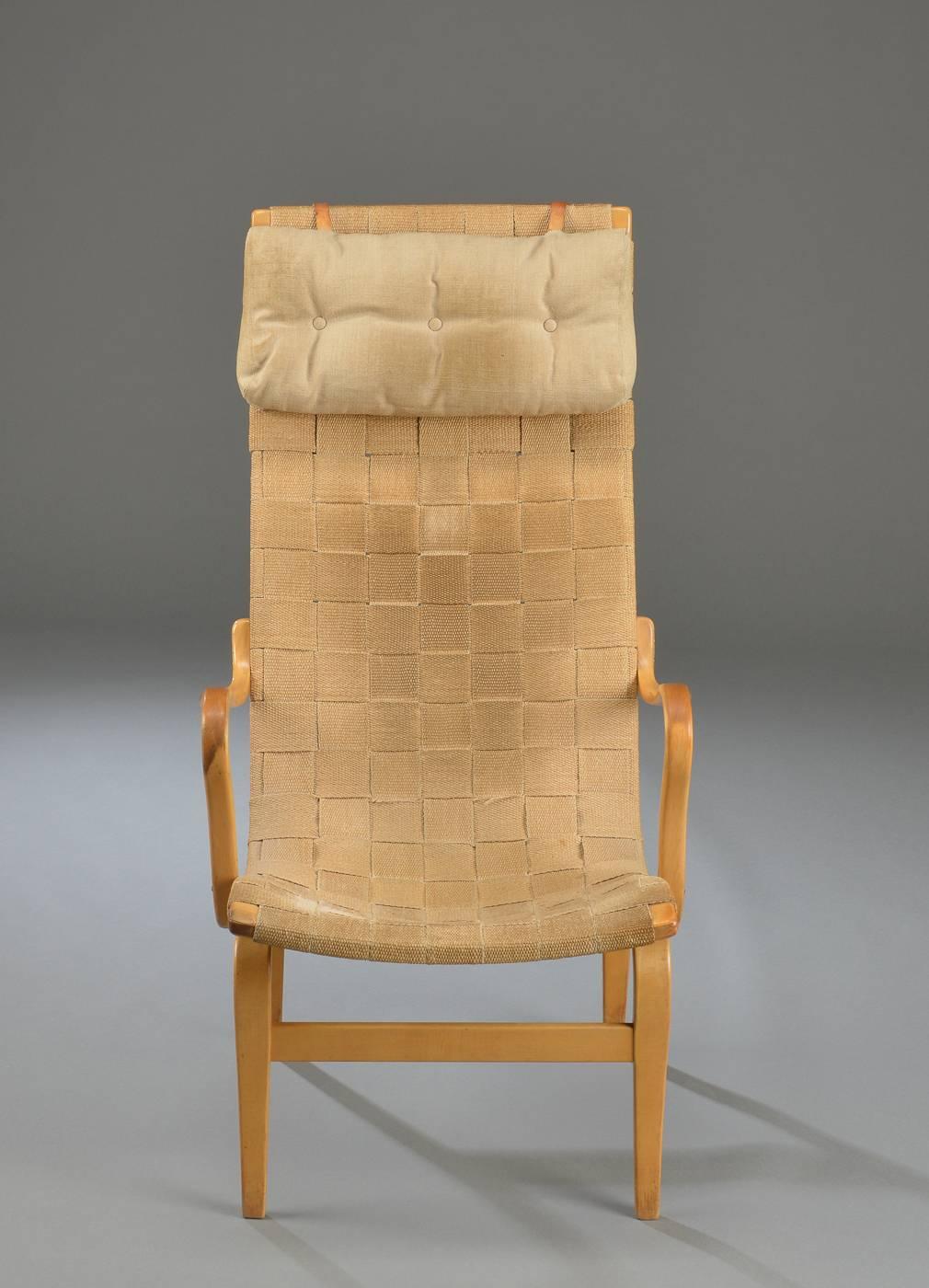 This Eva armchair by Bruno Mathsson was designed in 1969 and manufactured by Dux in Sweden. The chair features a molded beech frame, fabric webbing, and a detachable head cushion.