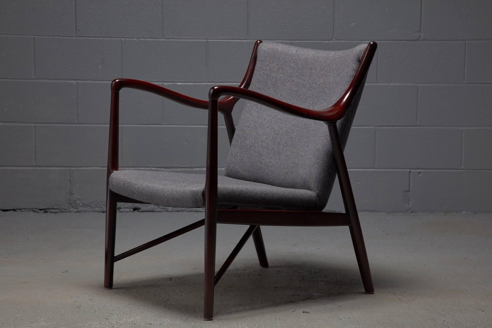 Designed in 1945 by Finn Juhl for a collaboration with Niels Vodder, the NV45 armchair is an iconic design. This armchair being offered is in the style of this widely sought after chair and features a polished rosewood-colored wood frame and grey