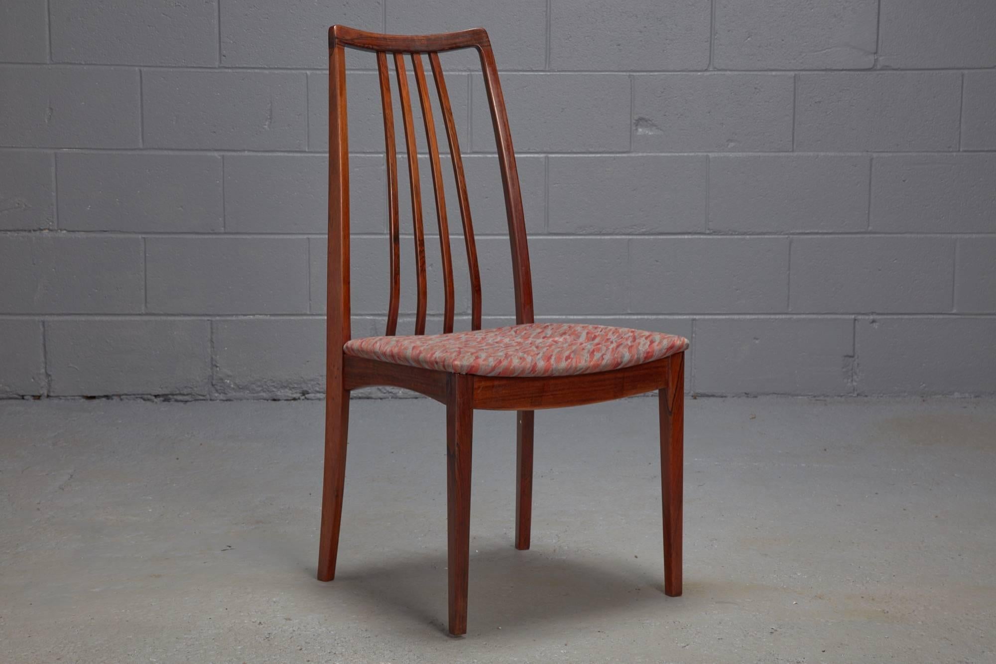These dining chairs feature an sculptural rosewood frame, an elegant high back with four thin spindles, and patterned upholstery. Sold as a set of four.
