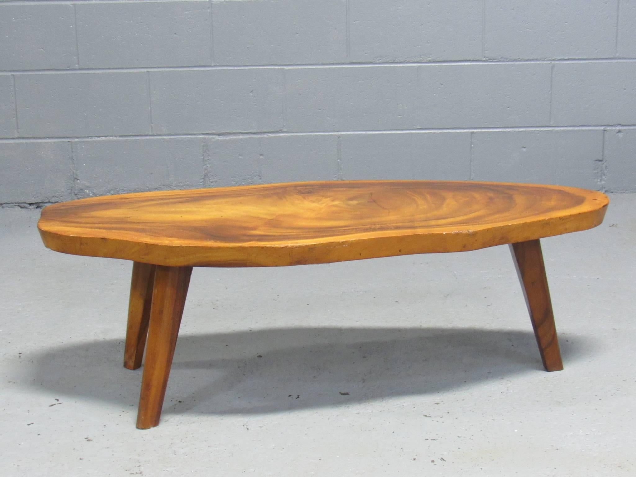 Standing on three legs, this unique Koa wood coffee table is crafted from a single piece of wood from the trunk of a Koa tree native to Hawaii.
