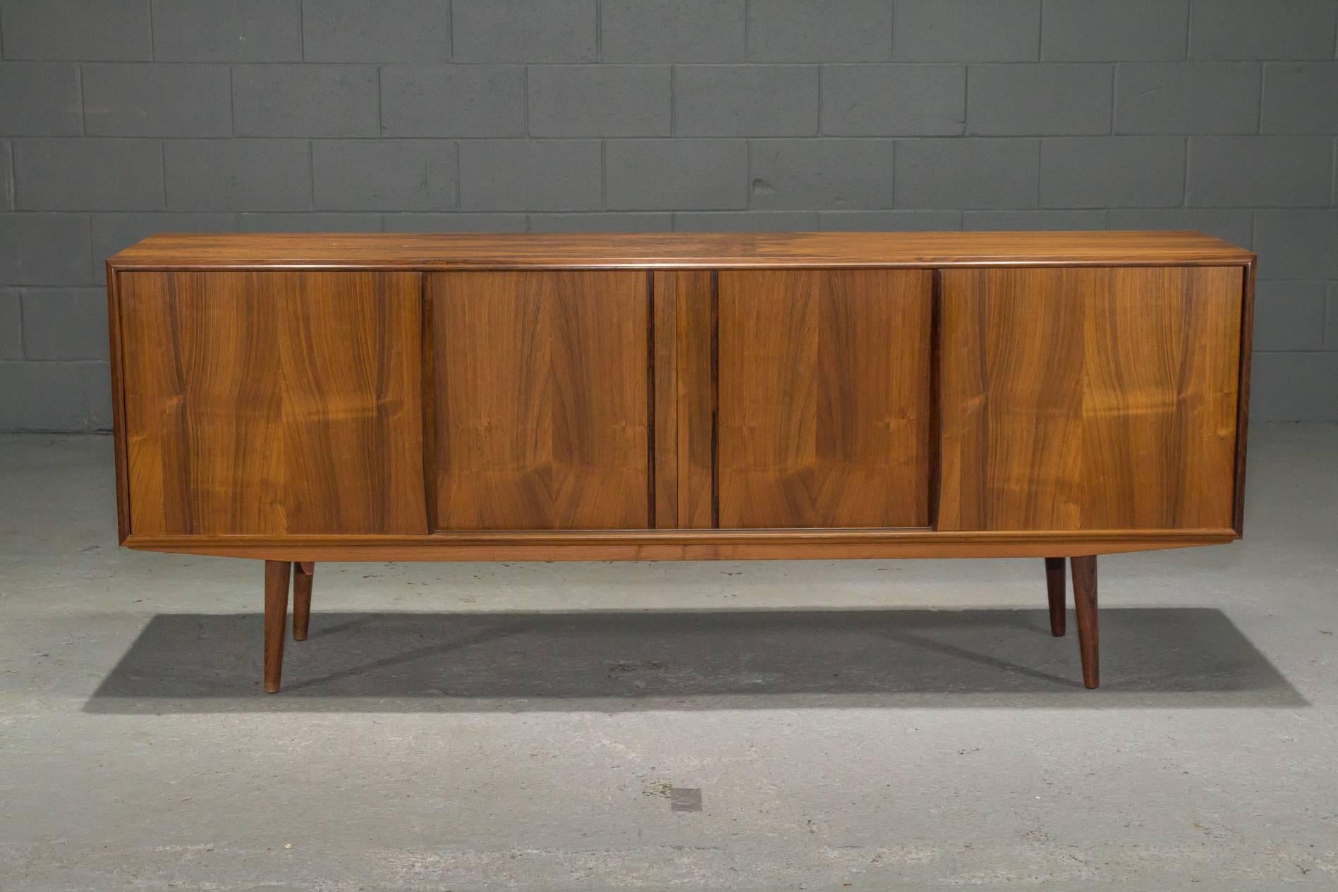 Danish modern midcentury rosewood sideboard. This sideboard features four sliding doors which open to reveal cutlery drawers on either side as well as an adjustable shelf on one side, and a larger adjustable shelf in the middle.