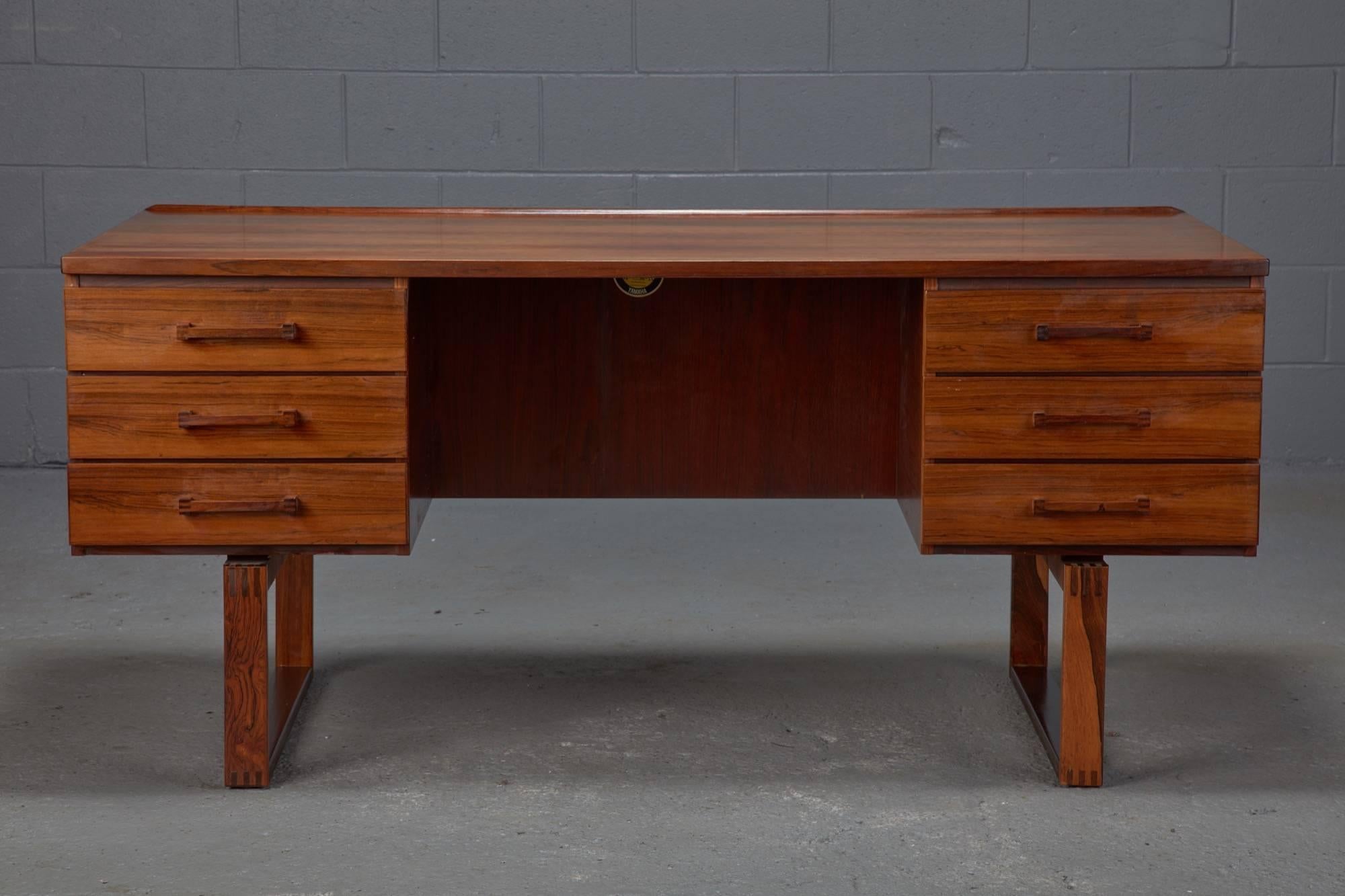 Designed in Denmark by Henning Jensen & Torben Valeur, this rosewood desk features a sled base, six drawers on the front and a storage compartment shelf at the rear.